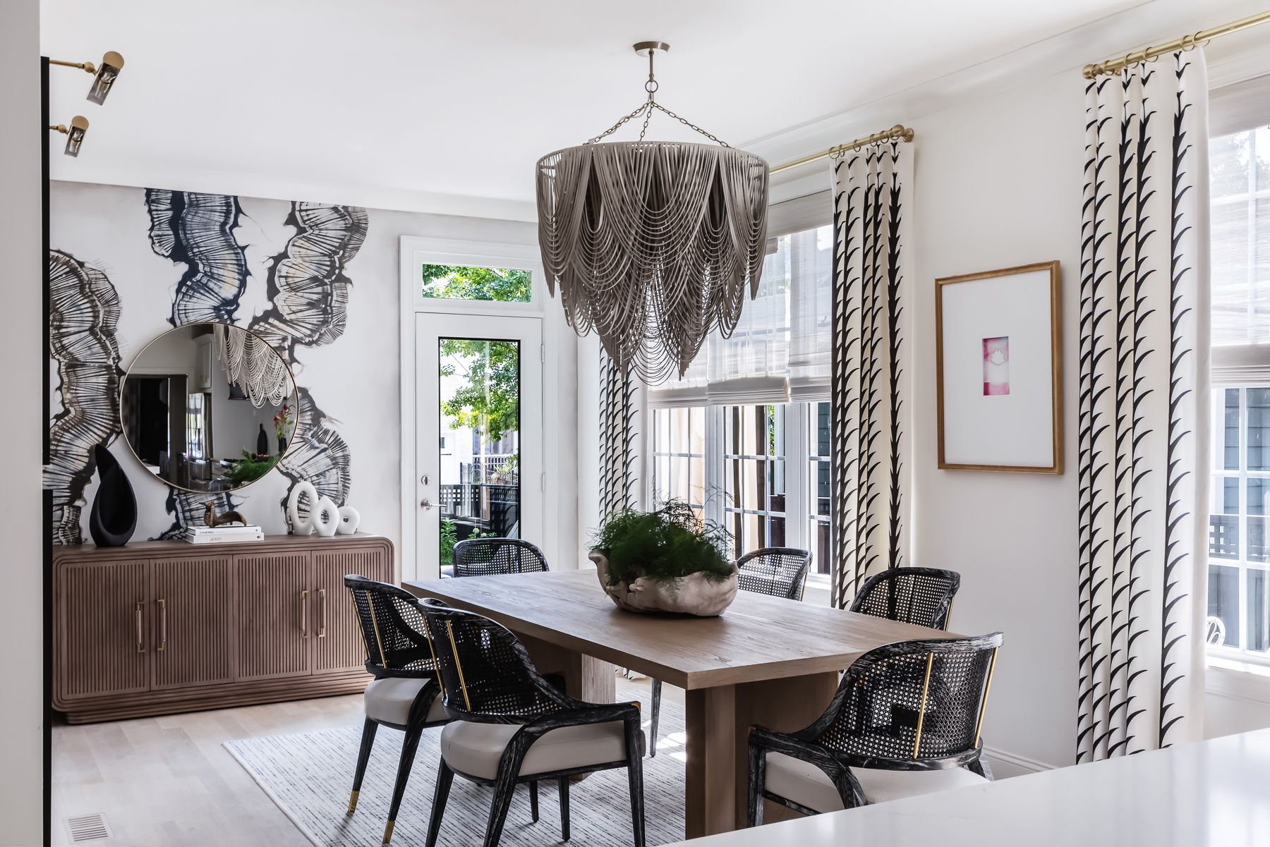 Dining room with wooden table, six chairs, large window, and decorative curtains, with a chandelier hanging from the ceiling.