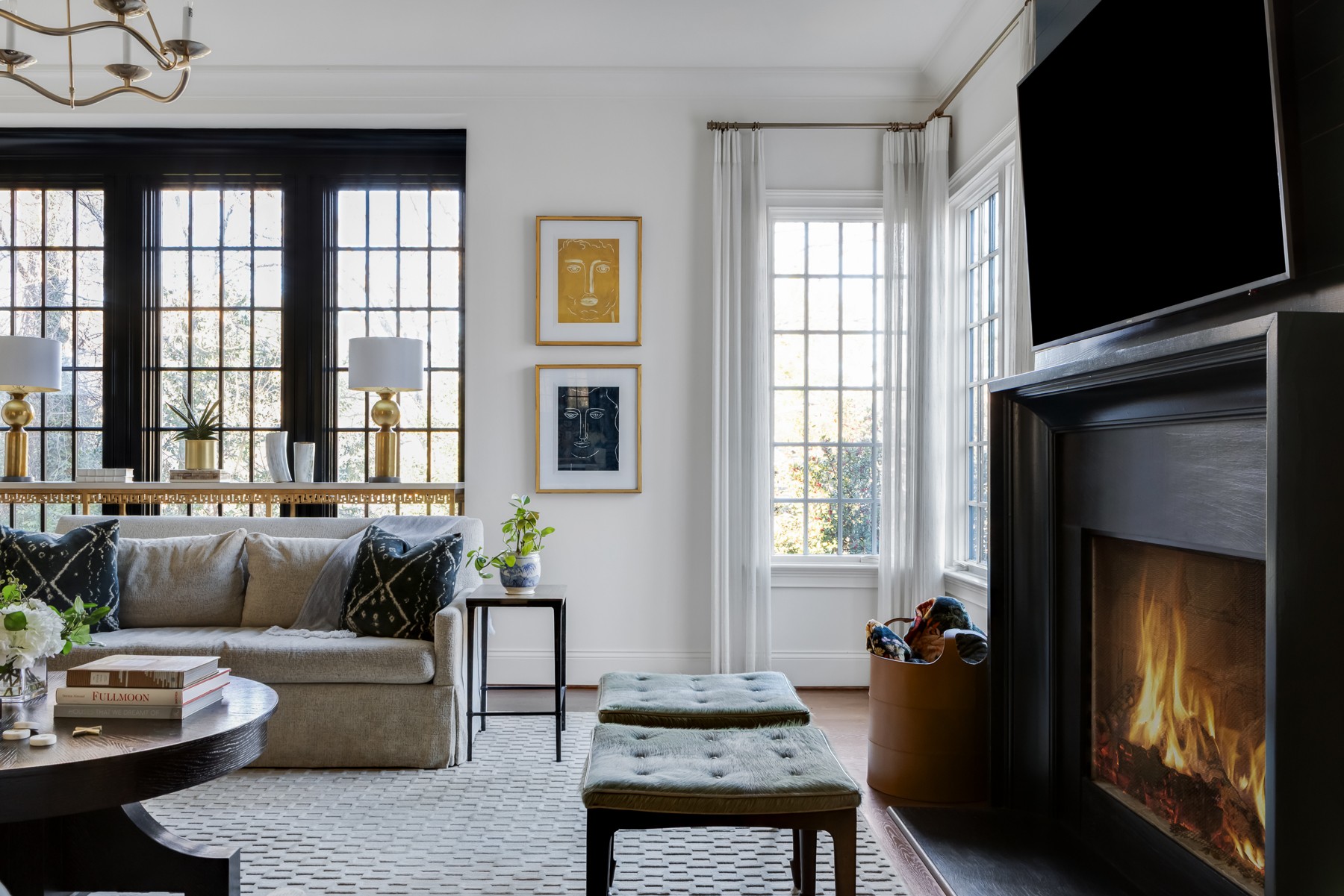 Living room with large windows, a sofa, fireplace, and wall-mounted TV, decorated with framed pictures and plants.