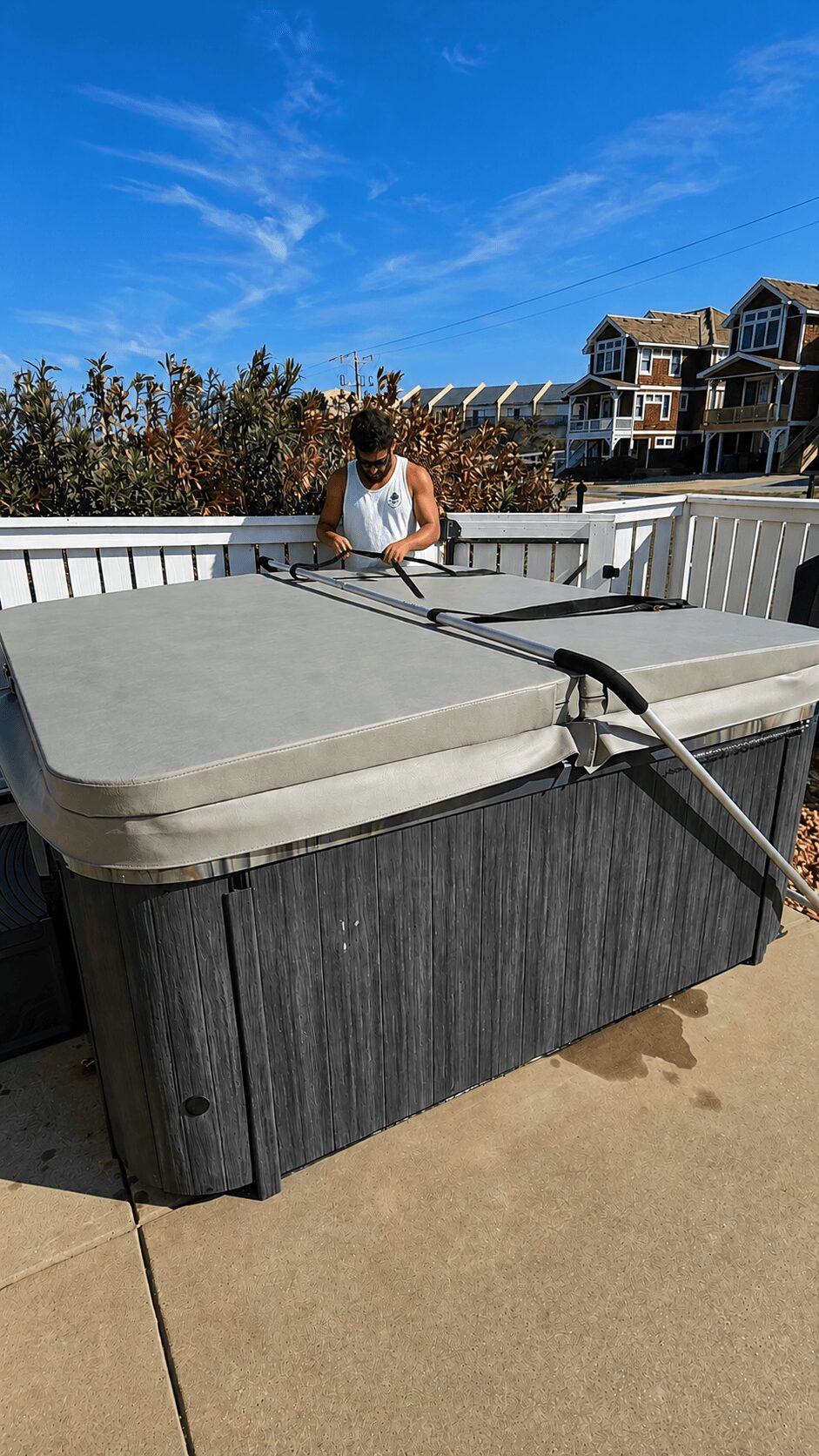 Person cleaning hot tub outdoors on a sunny day with houses and trees in background.