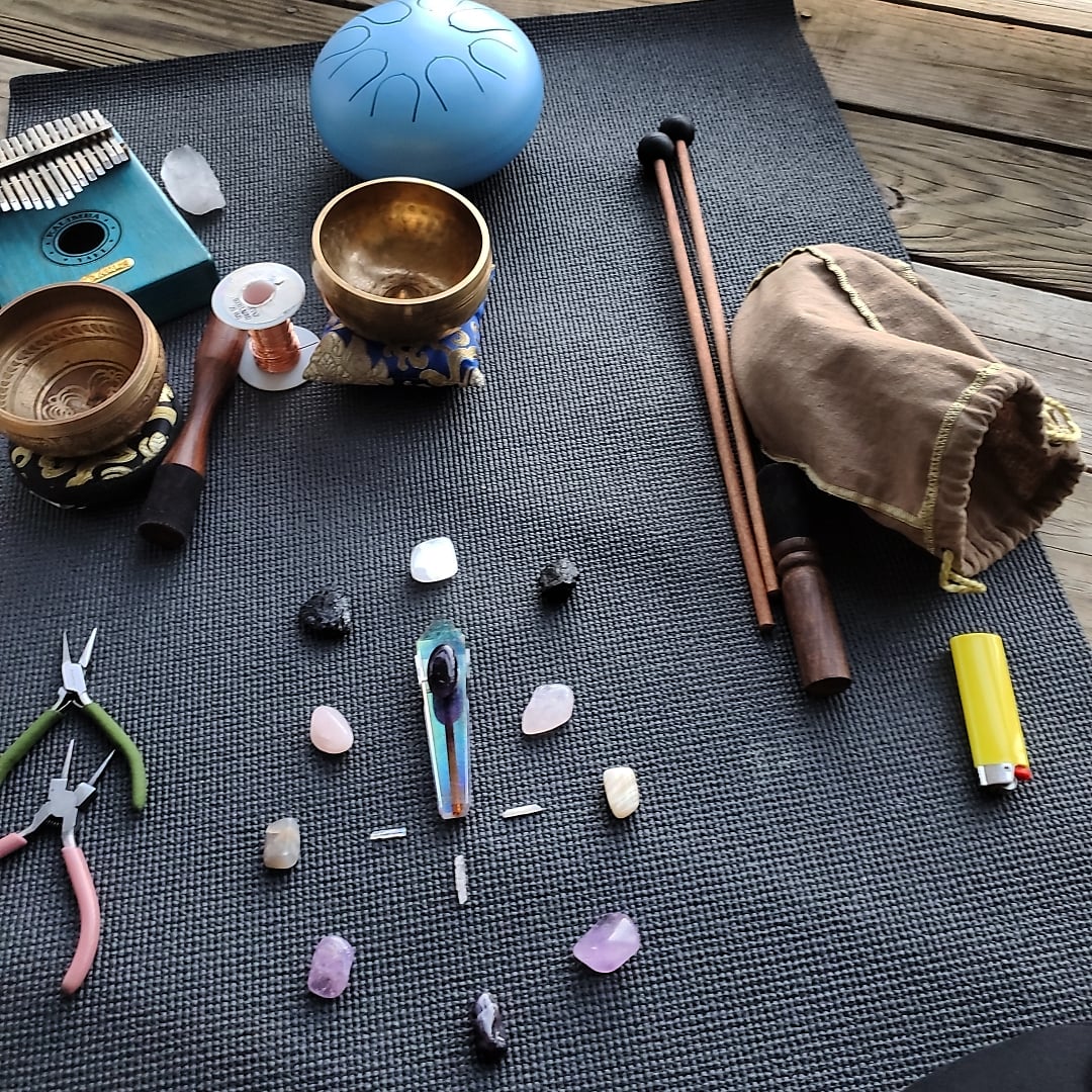 Yoga mat with singing bowls, a blue singing bowl, a small drum, a pouch, chopsticks, a lighter, and various stones.