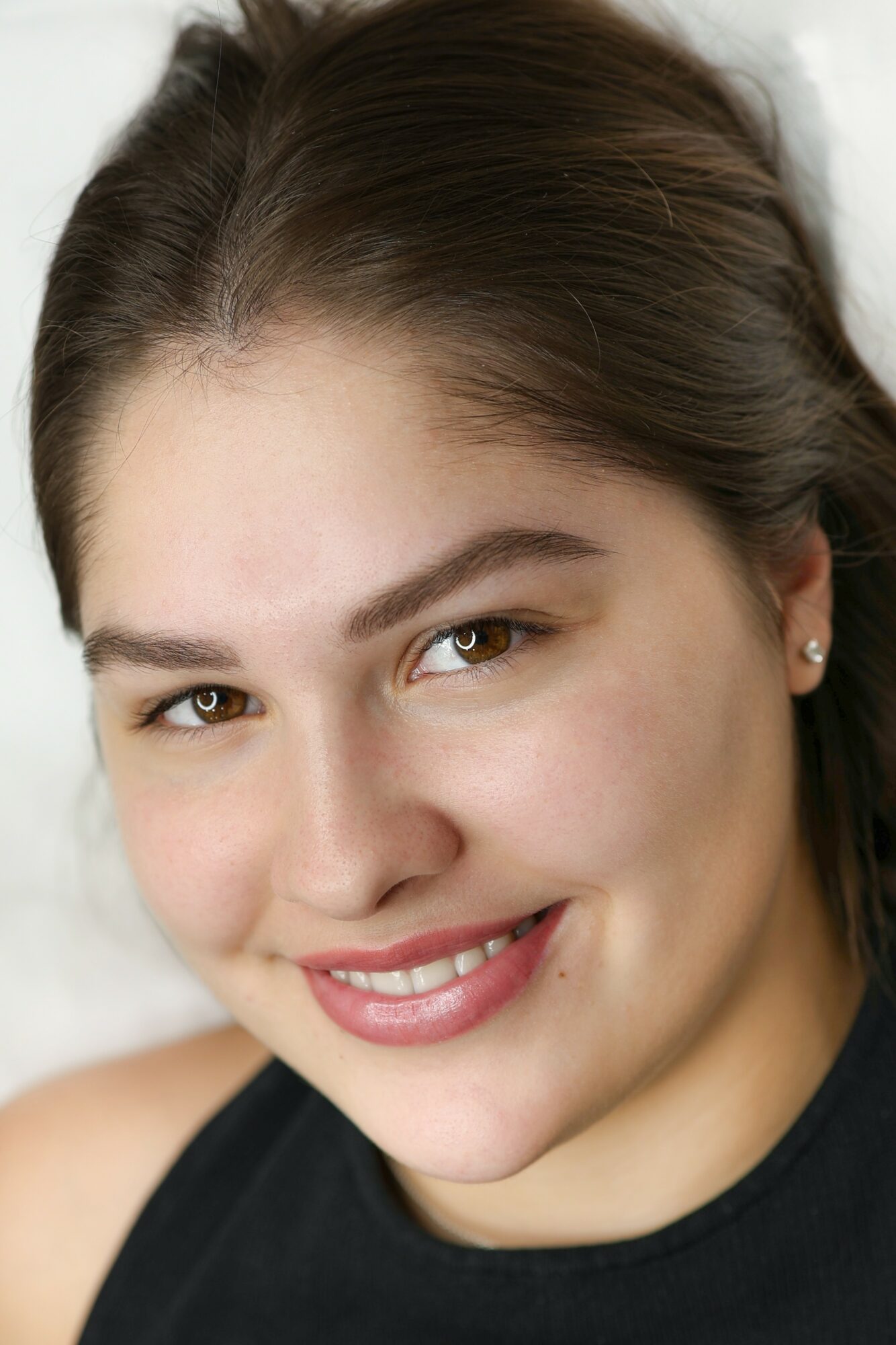 Close-up of a smiling young woman with brown hair and earrings, wearing a black top.
