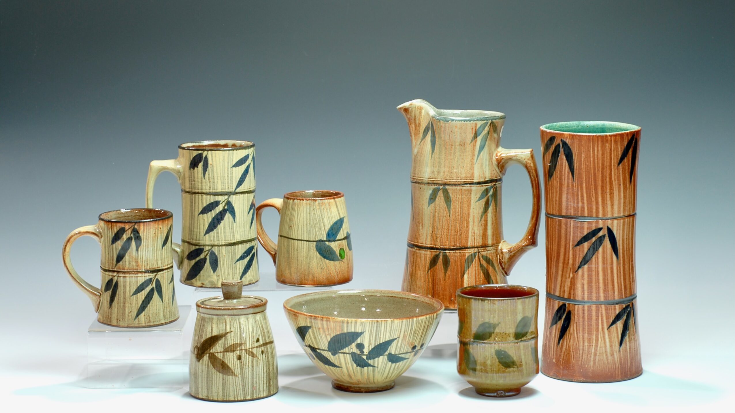 Collection of ceramic pitchers, cups, and bowls with bamboo leaf designs, arranged on a surface.