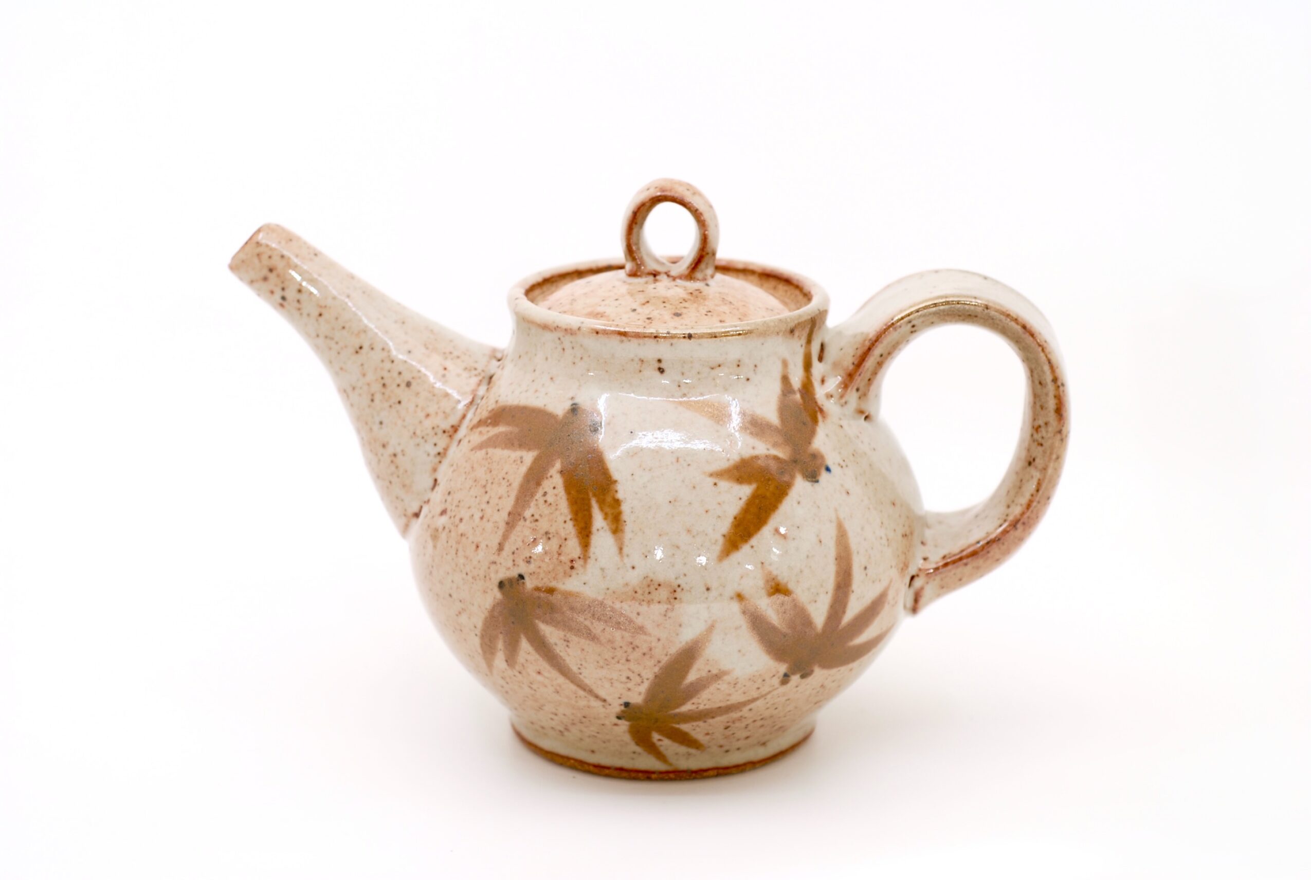Ceramic teapot with a round body, spout, handle, and a lid, decorated with brown leaf patterns on a white background.