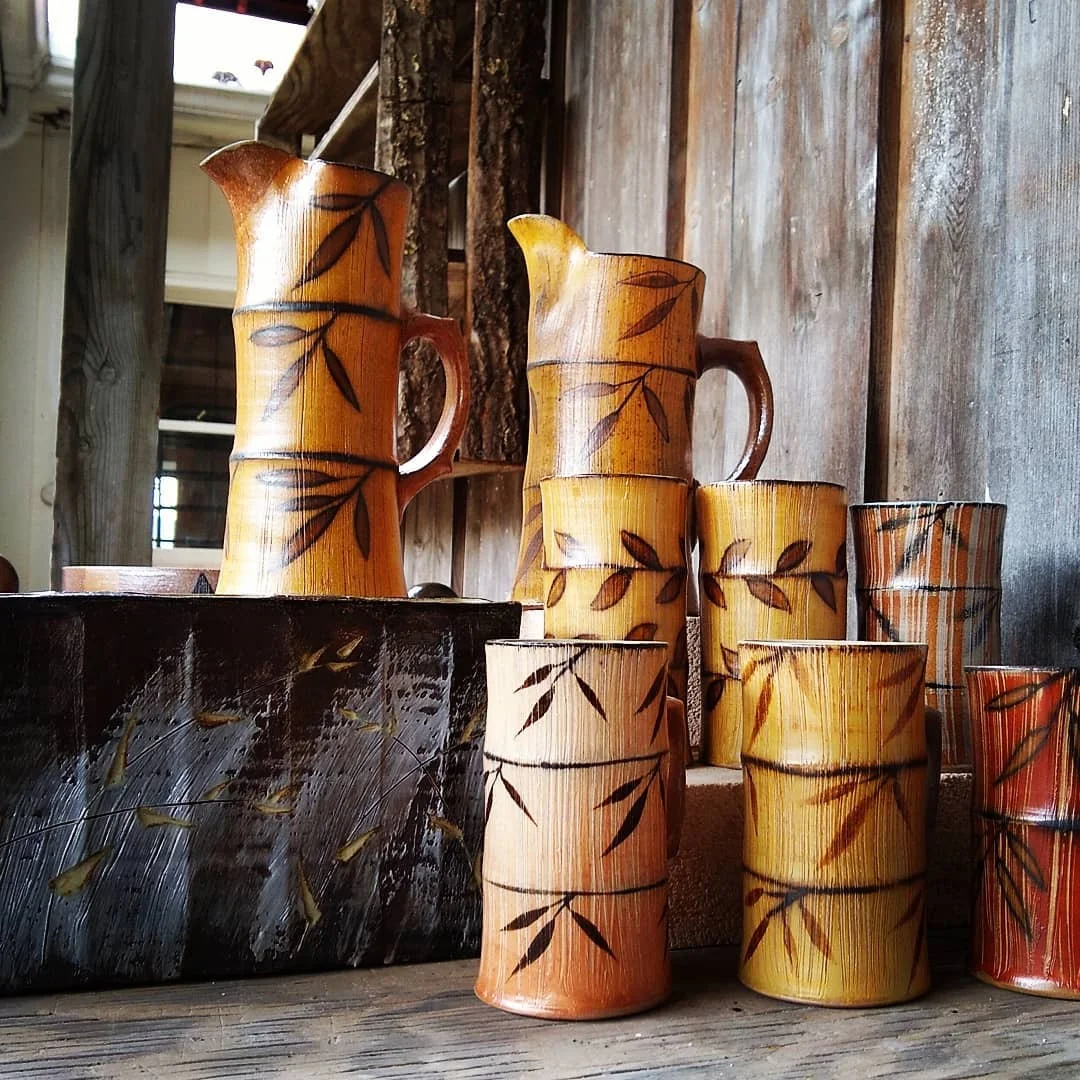 Collection of ceramic pitchers and cups with leaf patterns on a wooden surface and background.