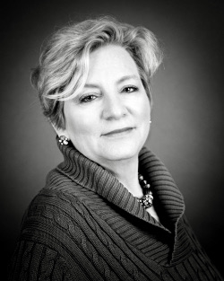 Black and white portrait of a woman with short, wavy hair wearing a turtleneck sweater and earrings.