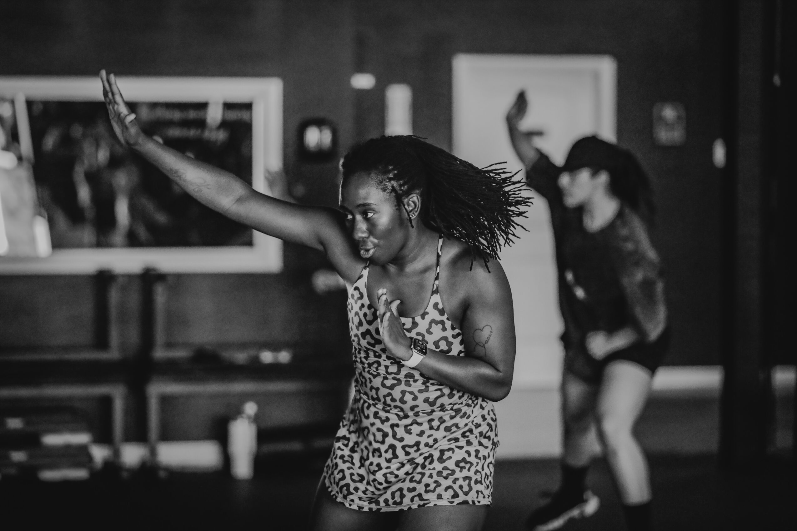 Two women dancing indoors, one in a leopard print dress with arm raised, the other in dark clothing in the background.