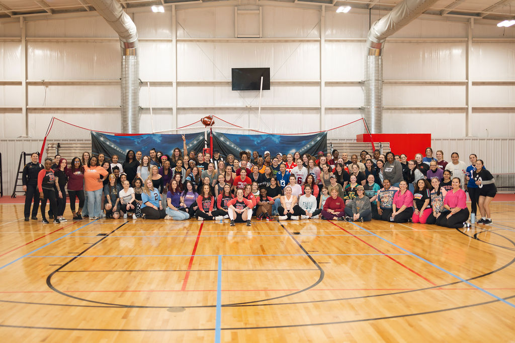 Large group of people gathered in a gymnasium, posing for a photo in front of a volleyball net and sports equipment.