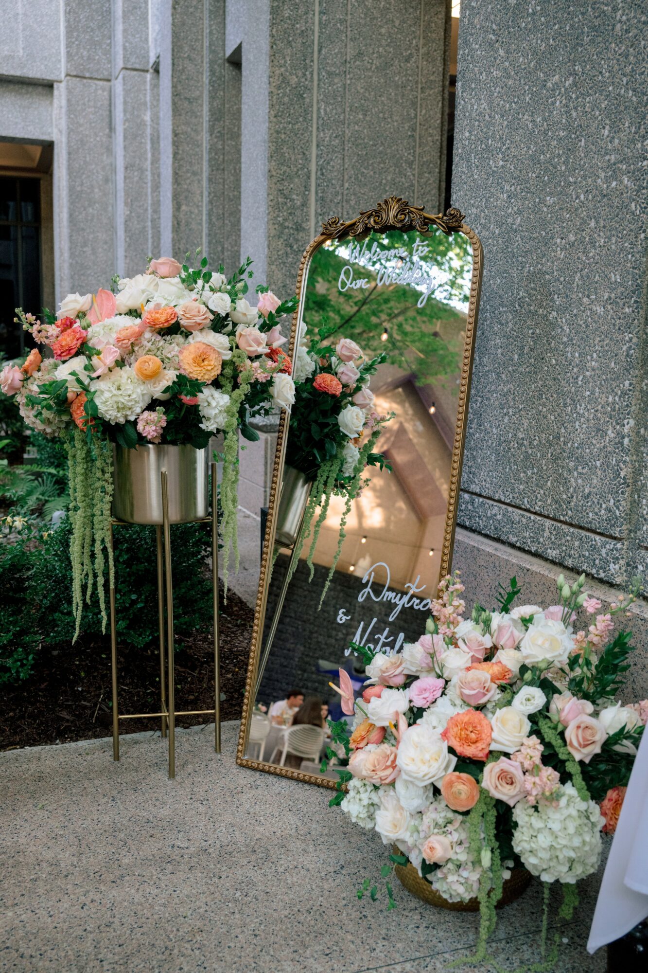 Flower arrangements and a mirror with floral decorations leaning against a wall, in an indoor setting.
