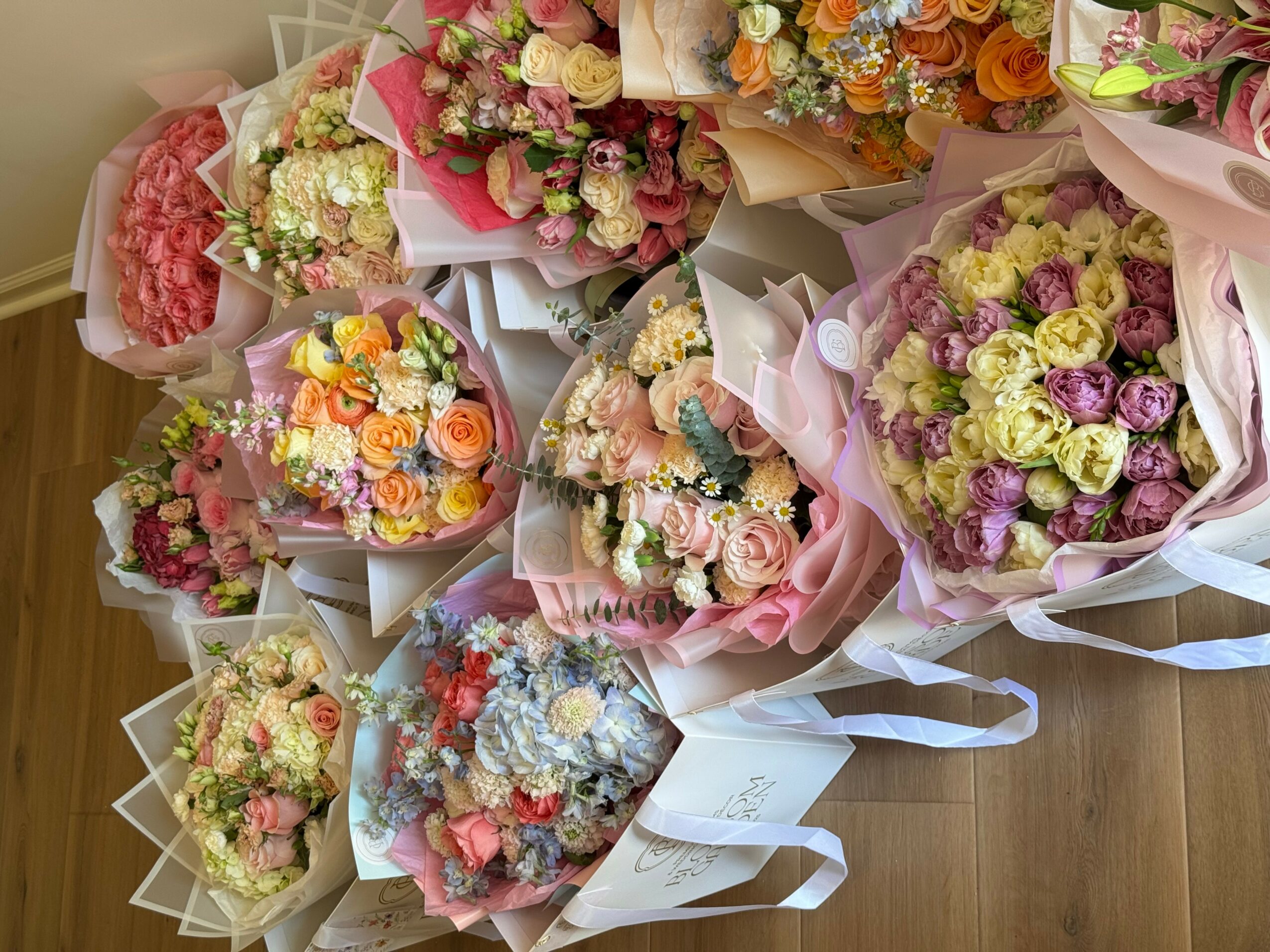 Multiple bouquets of colorful flowers arranged on a wooden surface, wrapped in paper and ribbons.