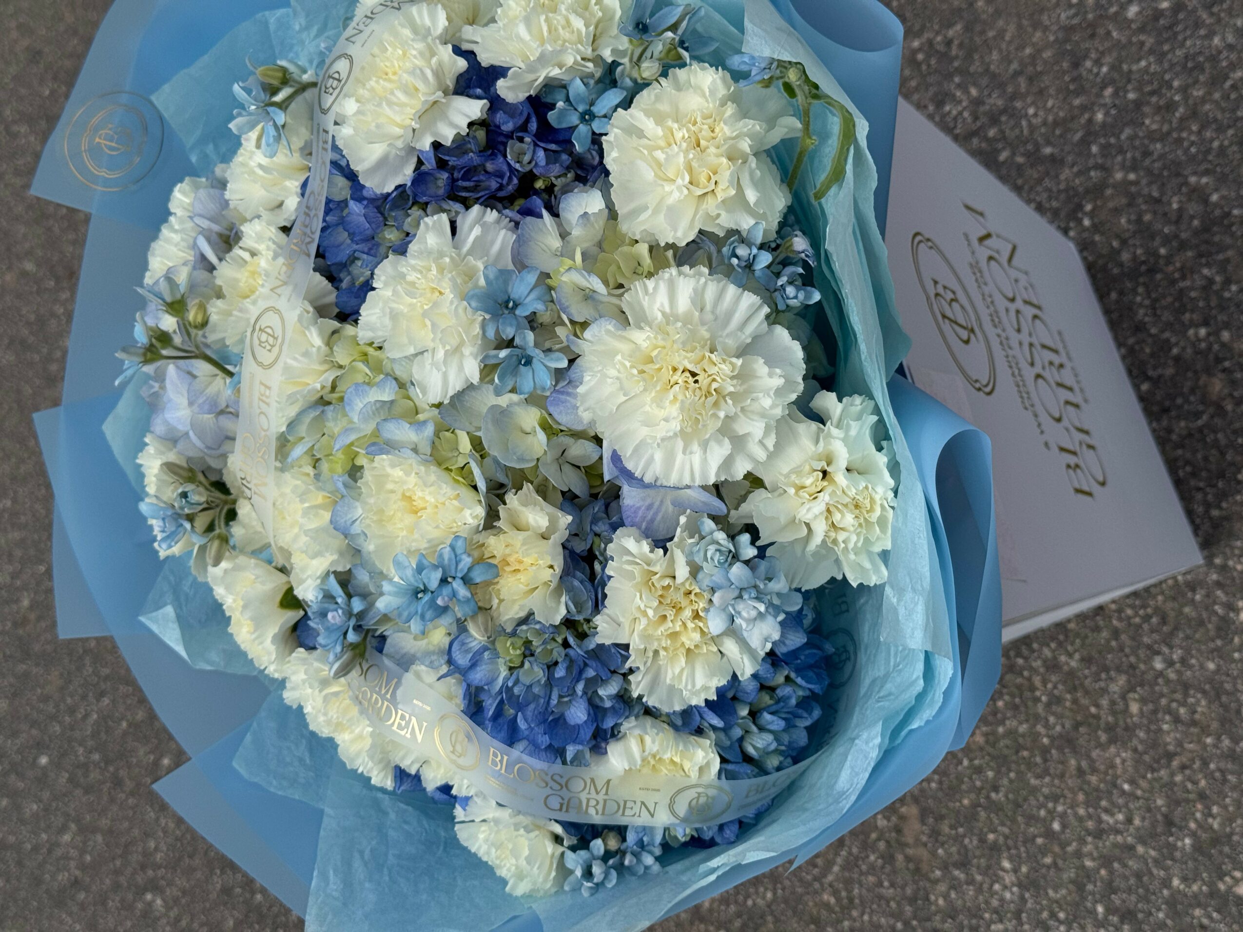 Bouquet of white and blue flowers wrapped in blue paper, with a card nearby.