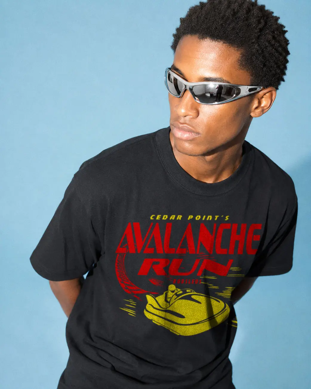 Young man wearing sunglasses and a black graphic T-shirt against a blue background.