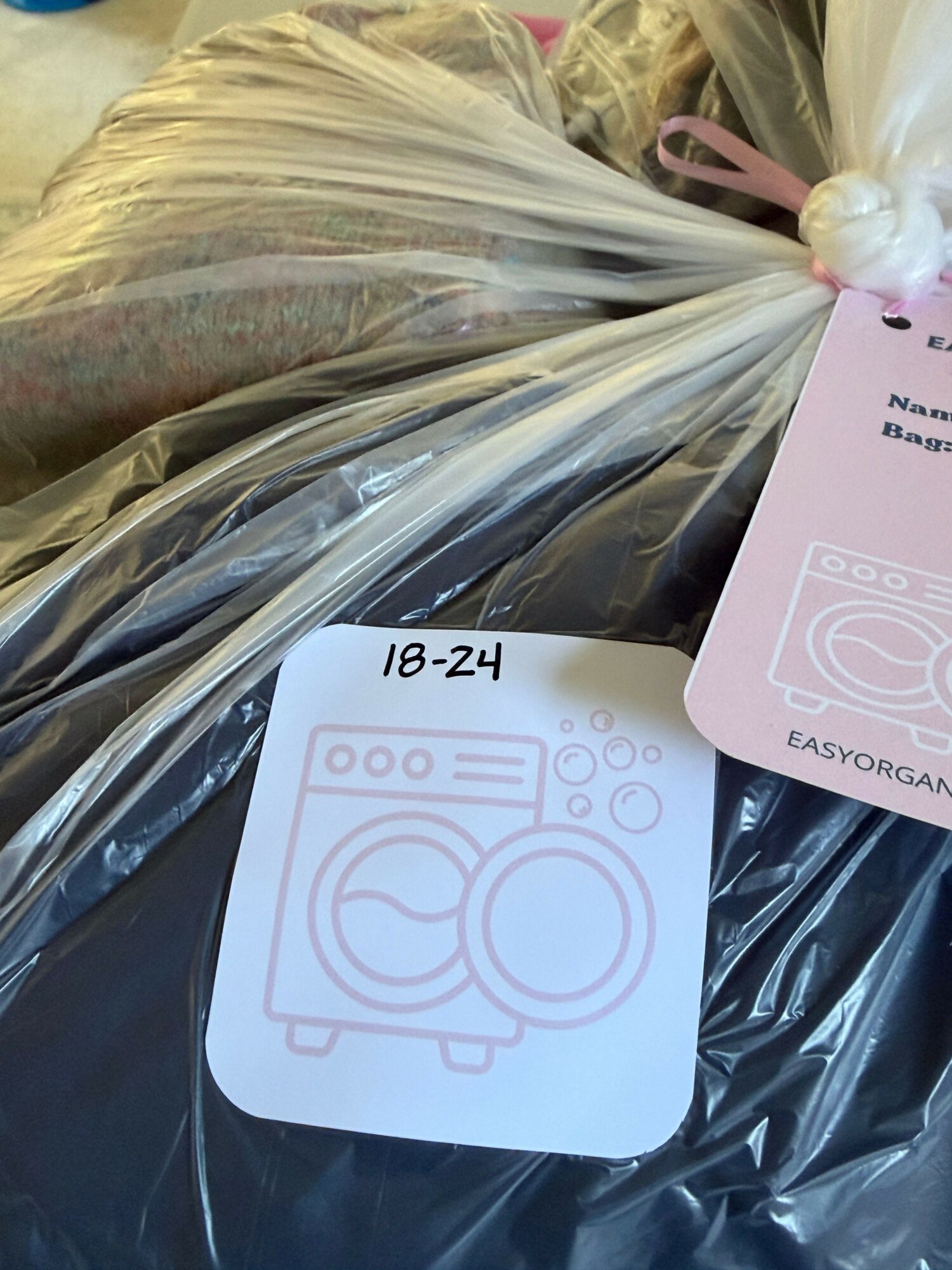 Plastic bag with a white tag attached, containing flowers and other items, with a second tag showing a camera icon and text.