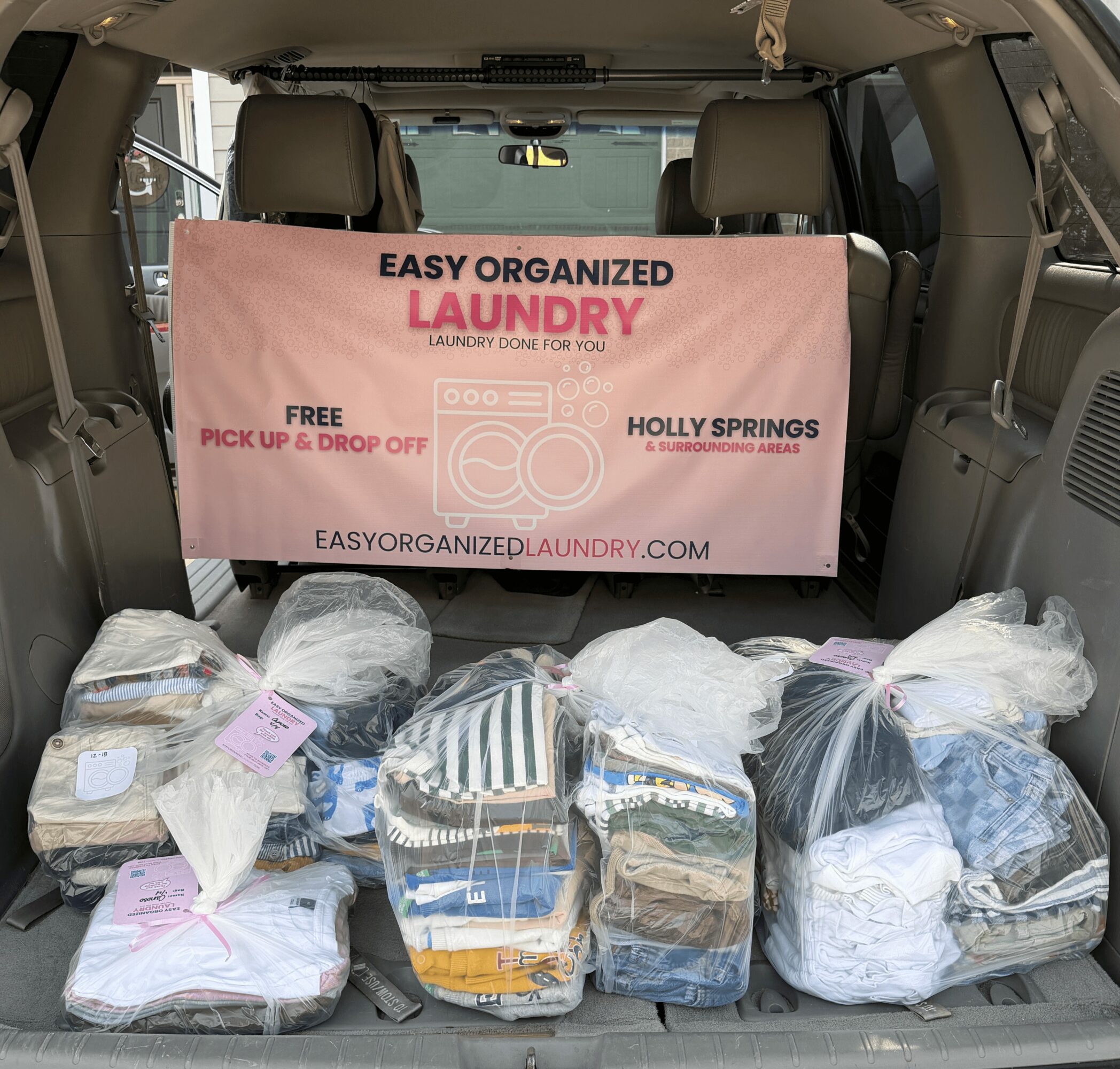 The back of a vehicle filled with bags of laundry and a pink sign advertising laundry services.
