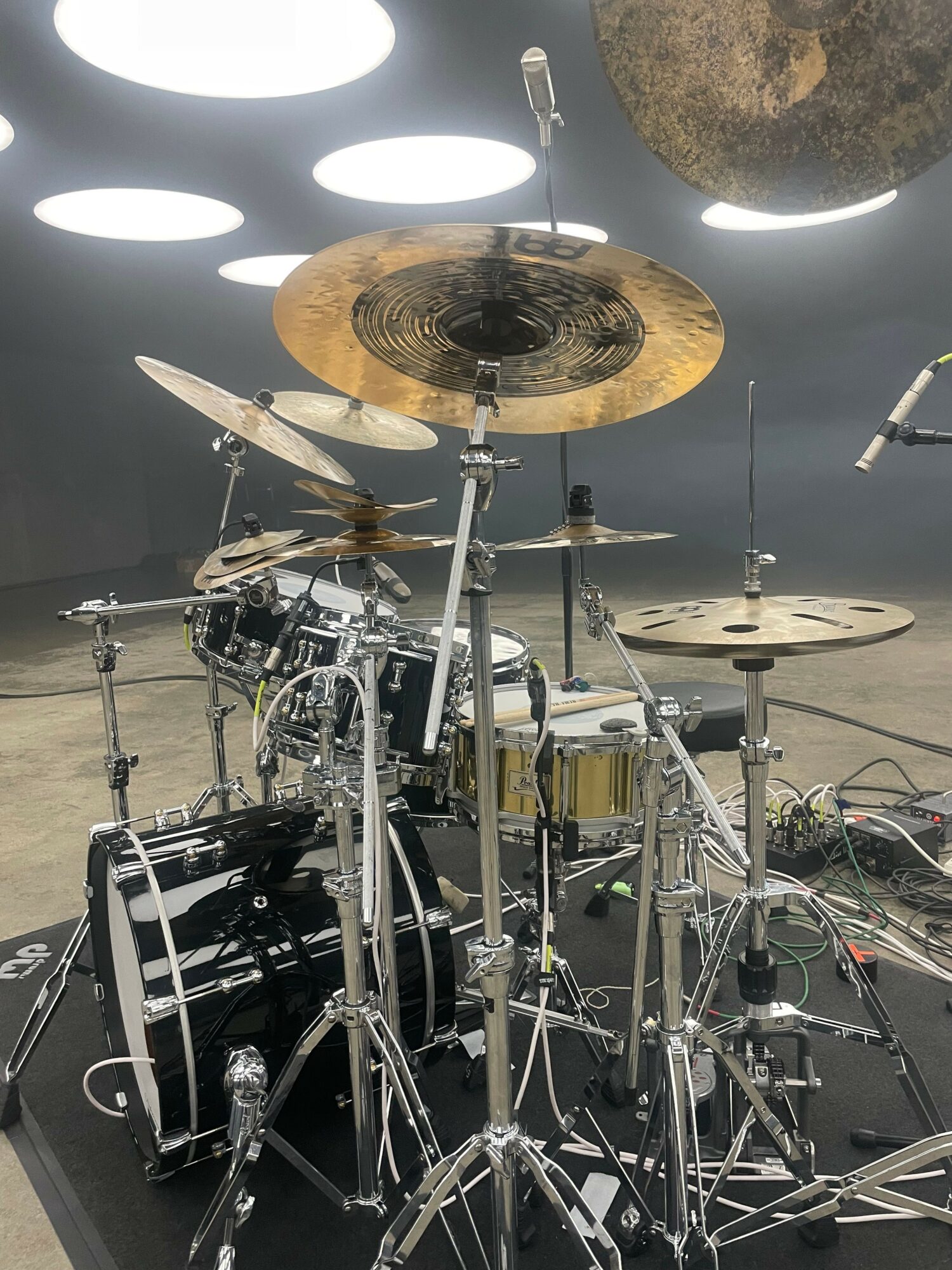 Drum set with cymbals and drums on a stage, with lighting and equipment in the background.