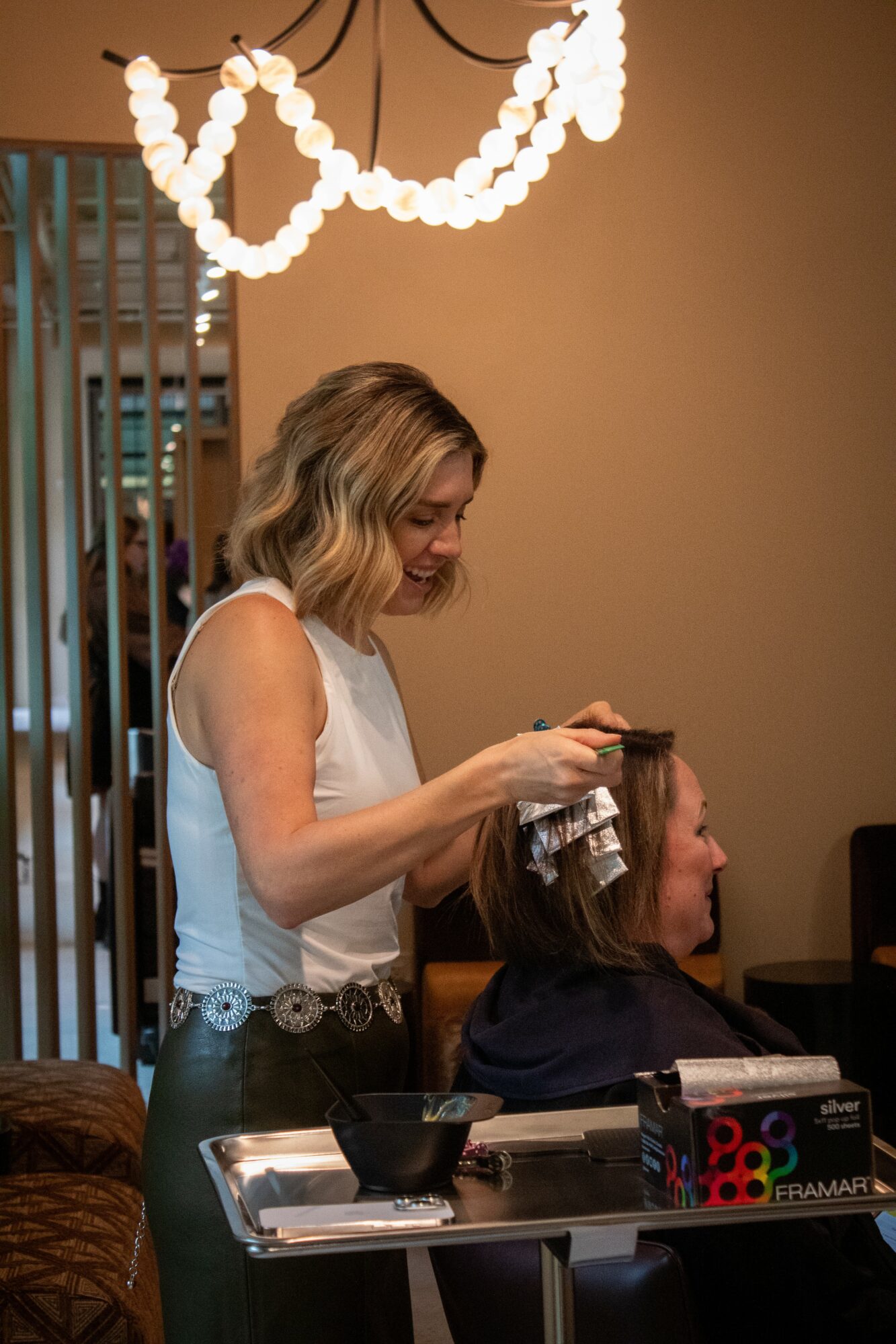 Woman styling a child's hair in a salon, with a string of lights hanging above, and salon tools on the table.