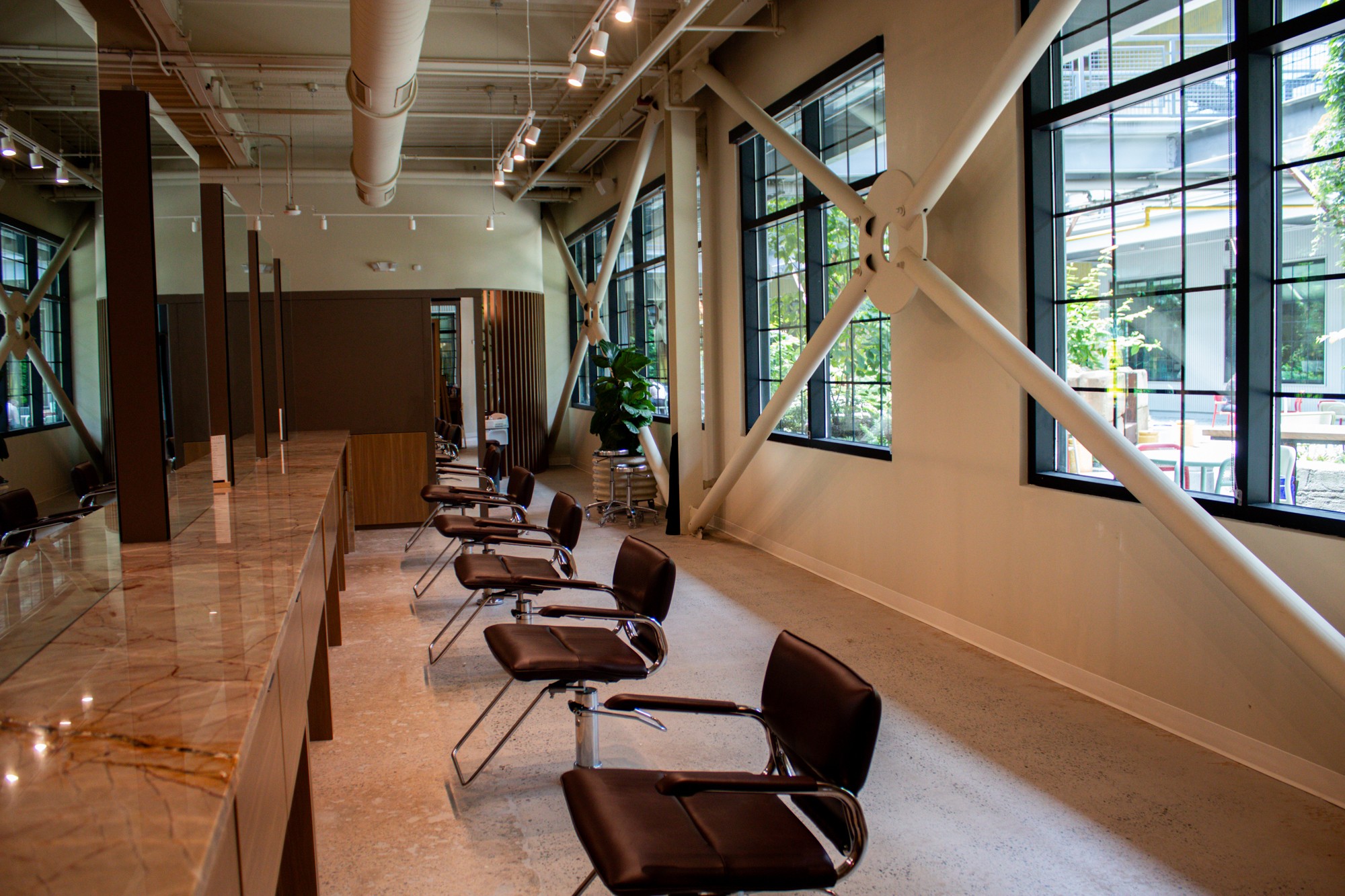Interior of a modern space with large windows, chairs along a wall, and a wooden counter, bright and airy.