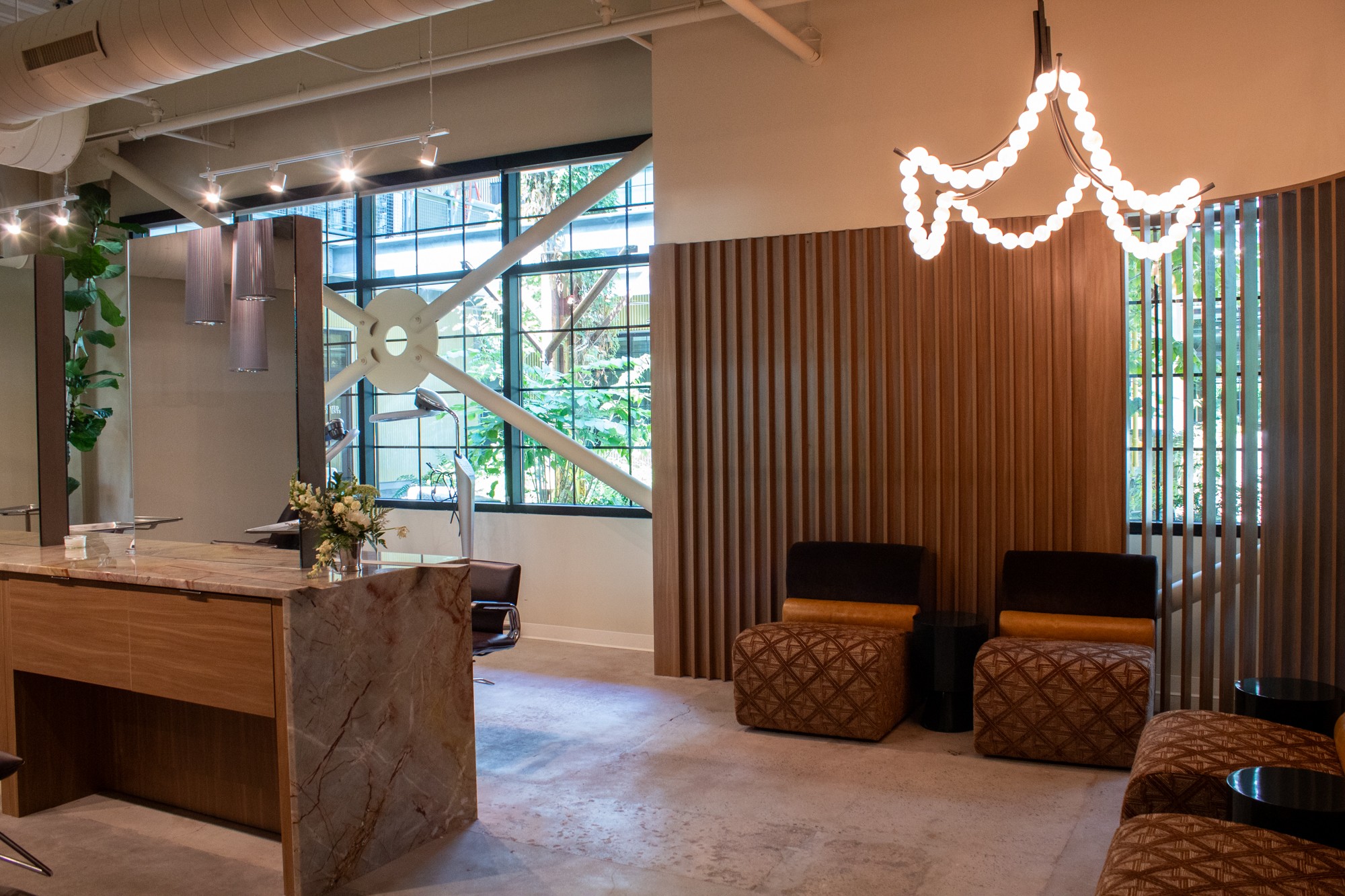 Modern interior with large window, wooden wall, seating area, and decorative lighting fixture, with a marble counter in the foreground.