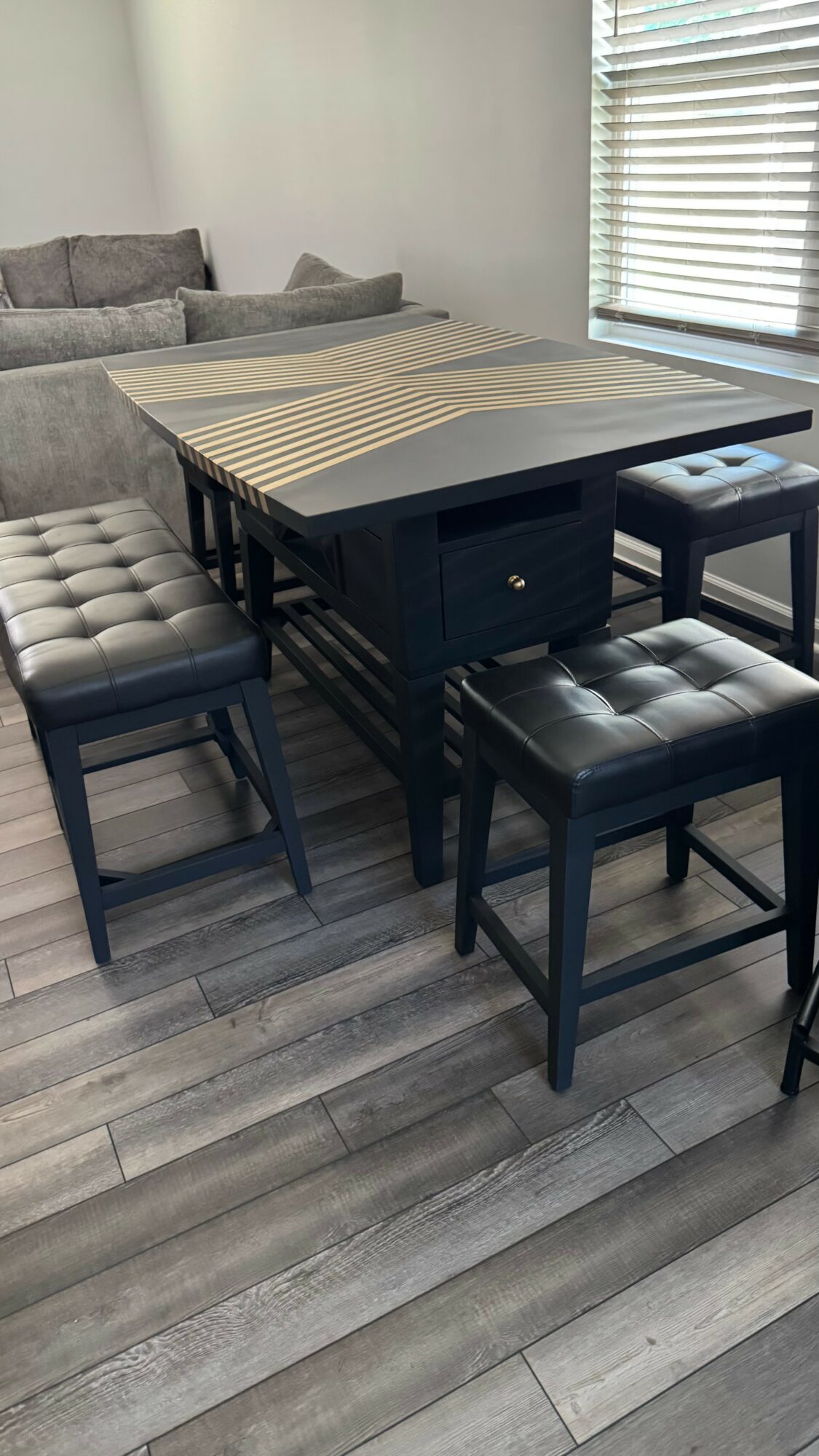 Dining table with four black cushioned stools in a room with a bed and window blinds.