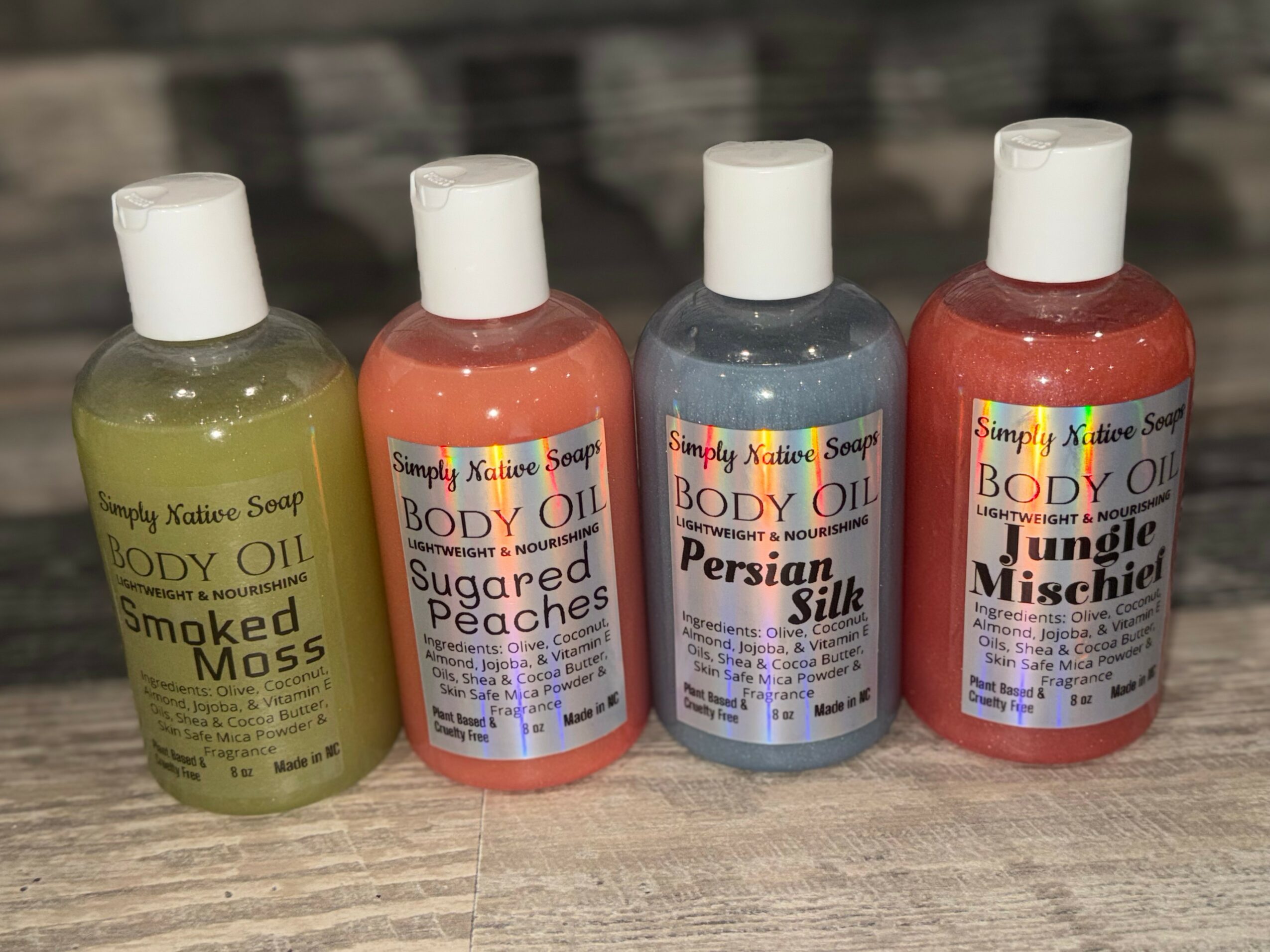 Four bottles of scented body oil with labels, placed on a wooden surface, background blurred, various colors and scents.