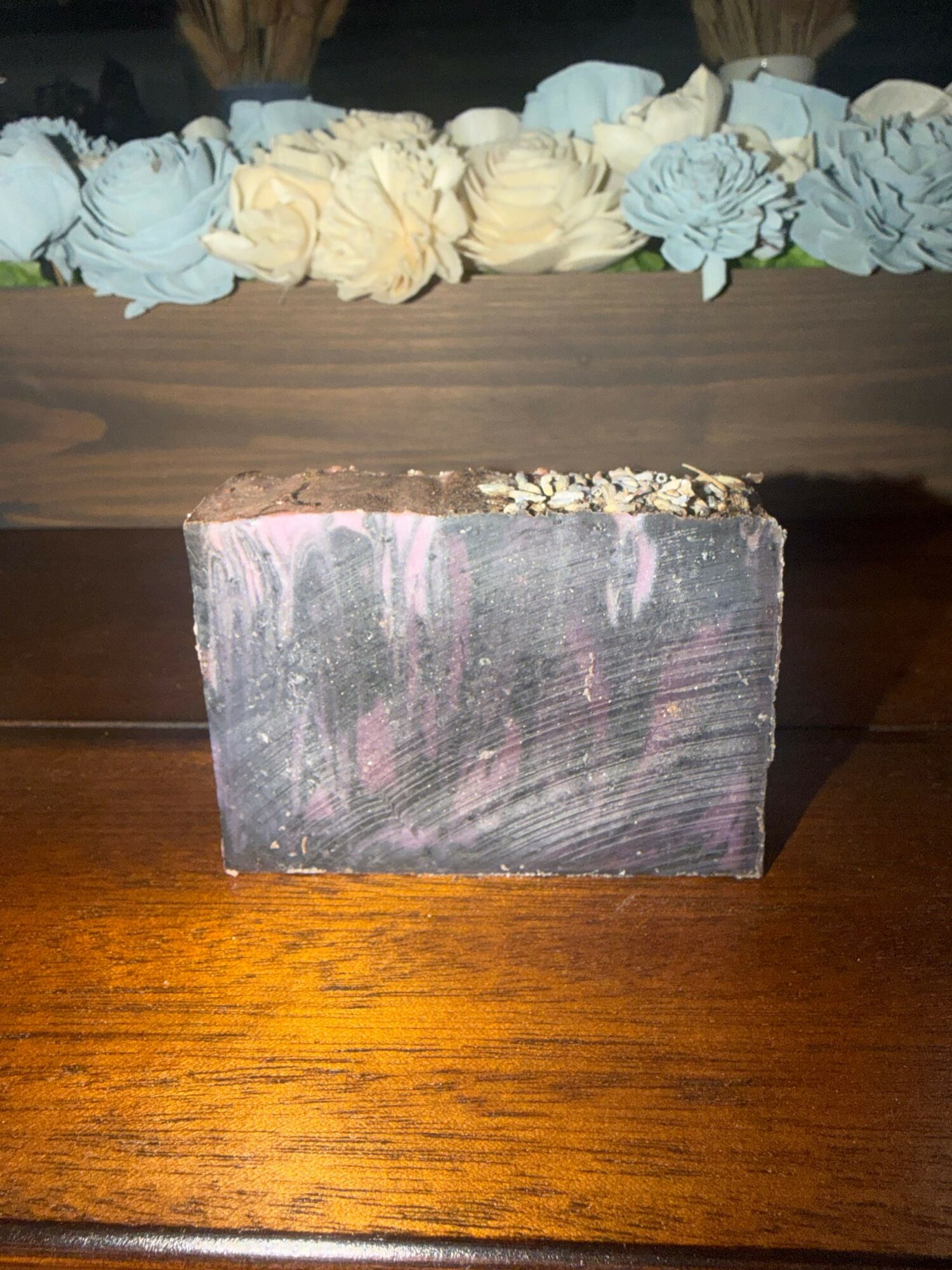 A rectangular object with a dark surface and pink streaks, placed on a wooden surface, with a decorative fabric border on the left.