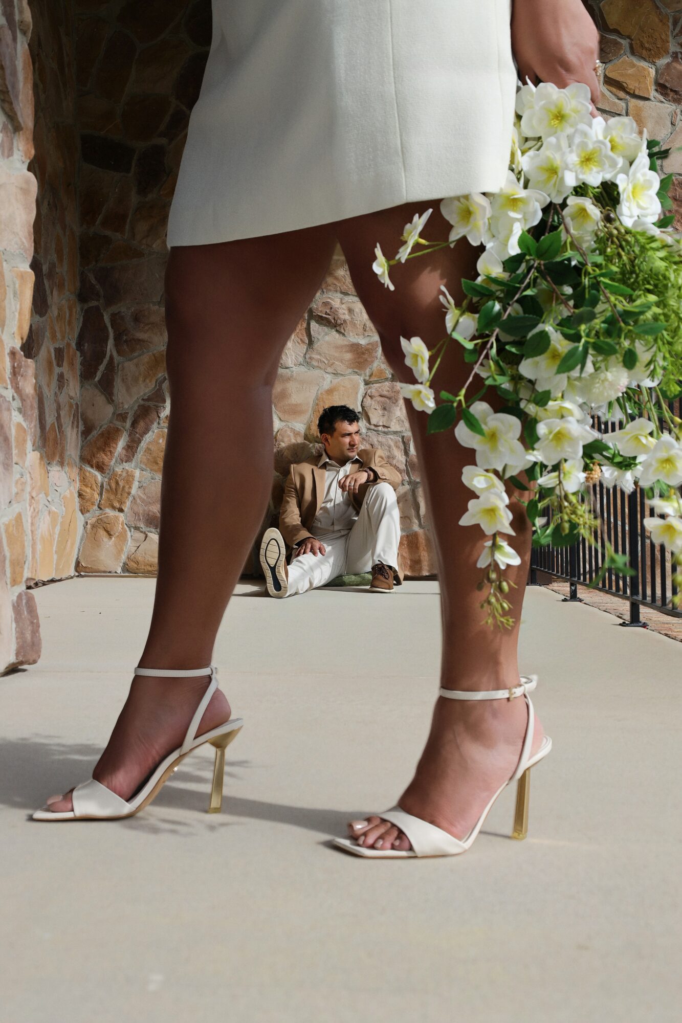 Person wearing white high-heeled sandals and a white dress, holding a bouquet of white flowers, standing outdoors.