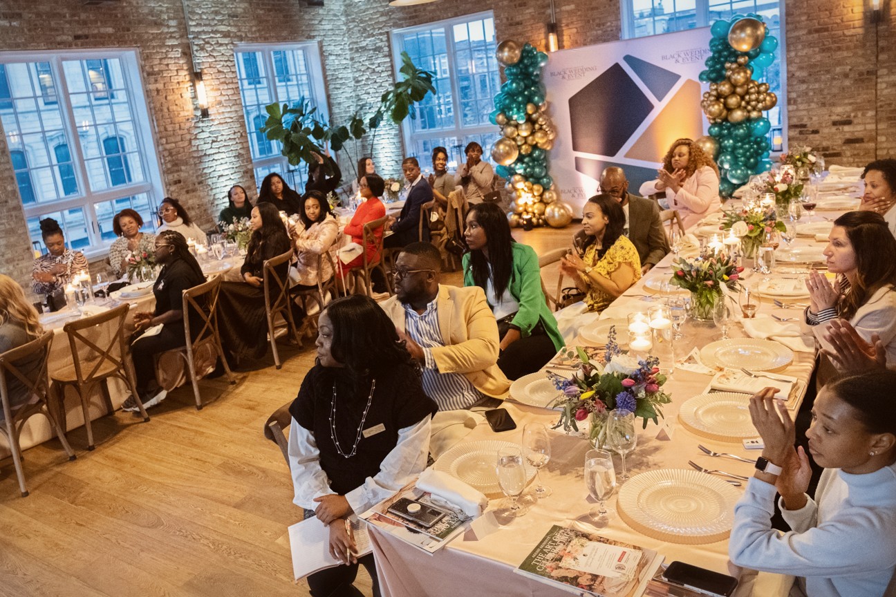 People seated at long decorated tables in a festive indoor setting with large windows and holiday decorations.