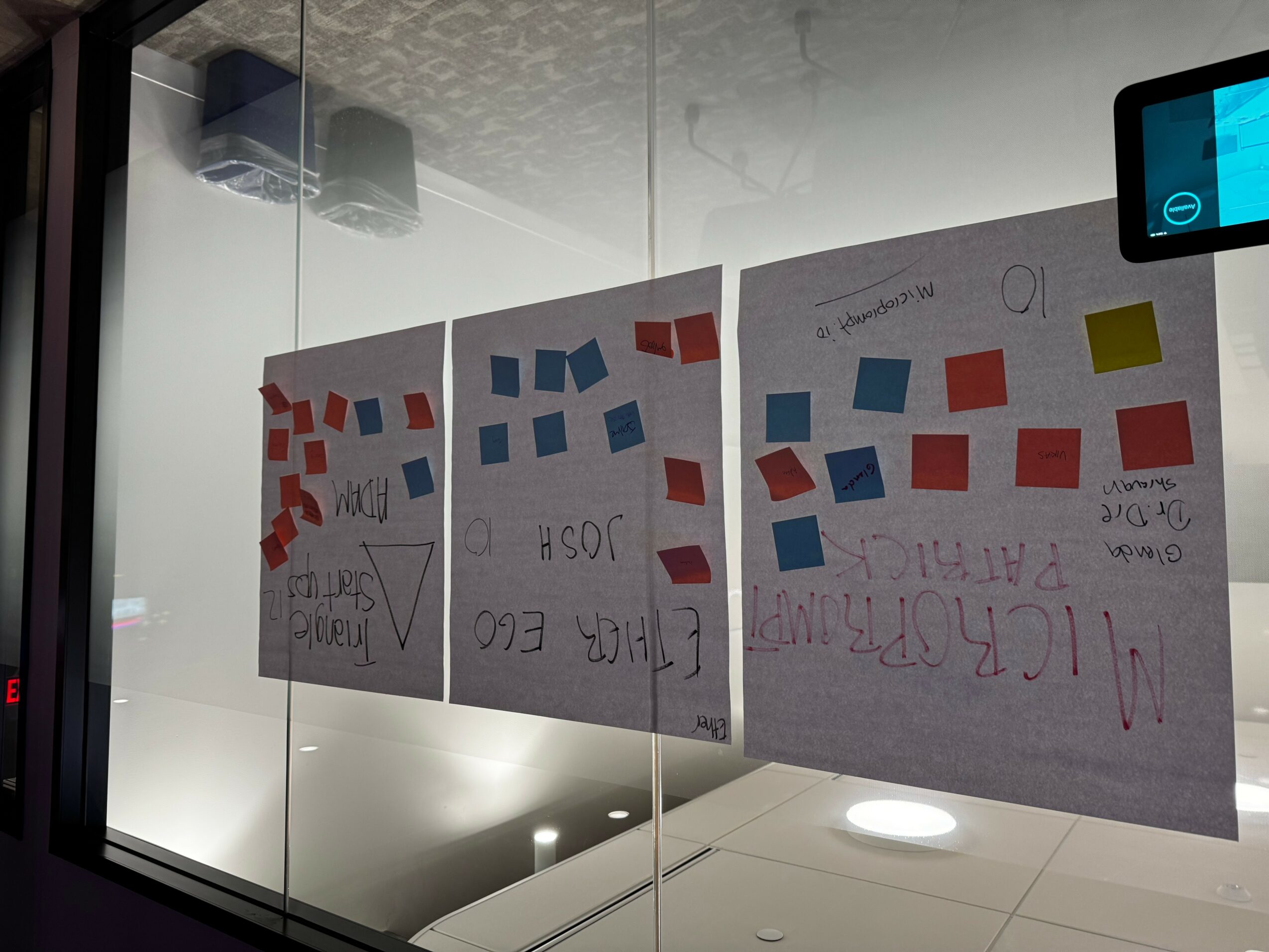 Two posters with red and blue squares and handwritten text are reflected in a glass window.