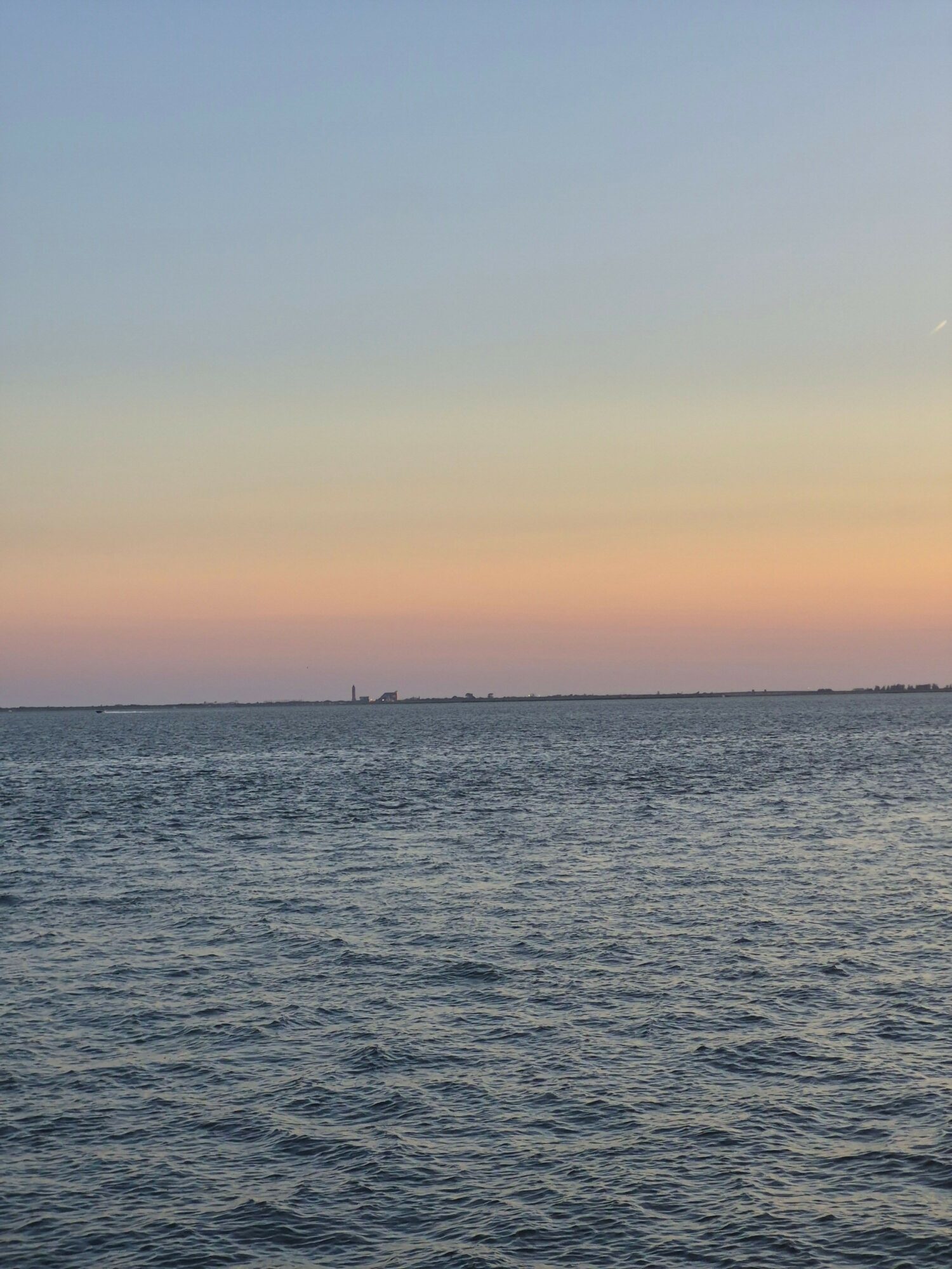 Sunset over water with colorful sky, horizon line visible, calm waves, and a distant city skyline.