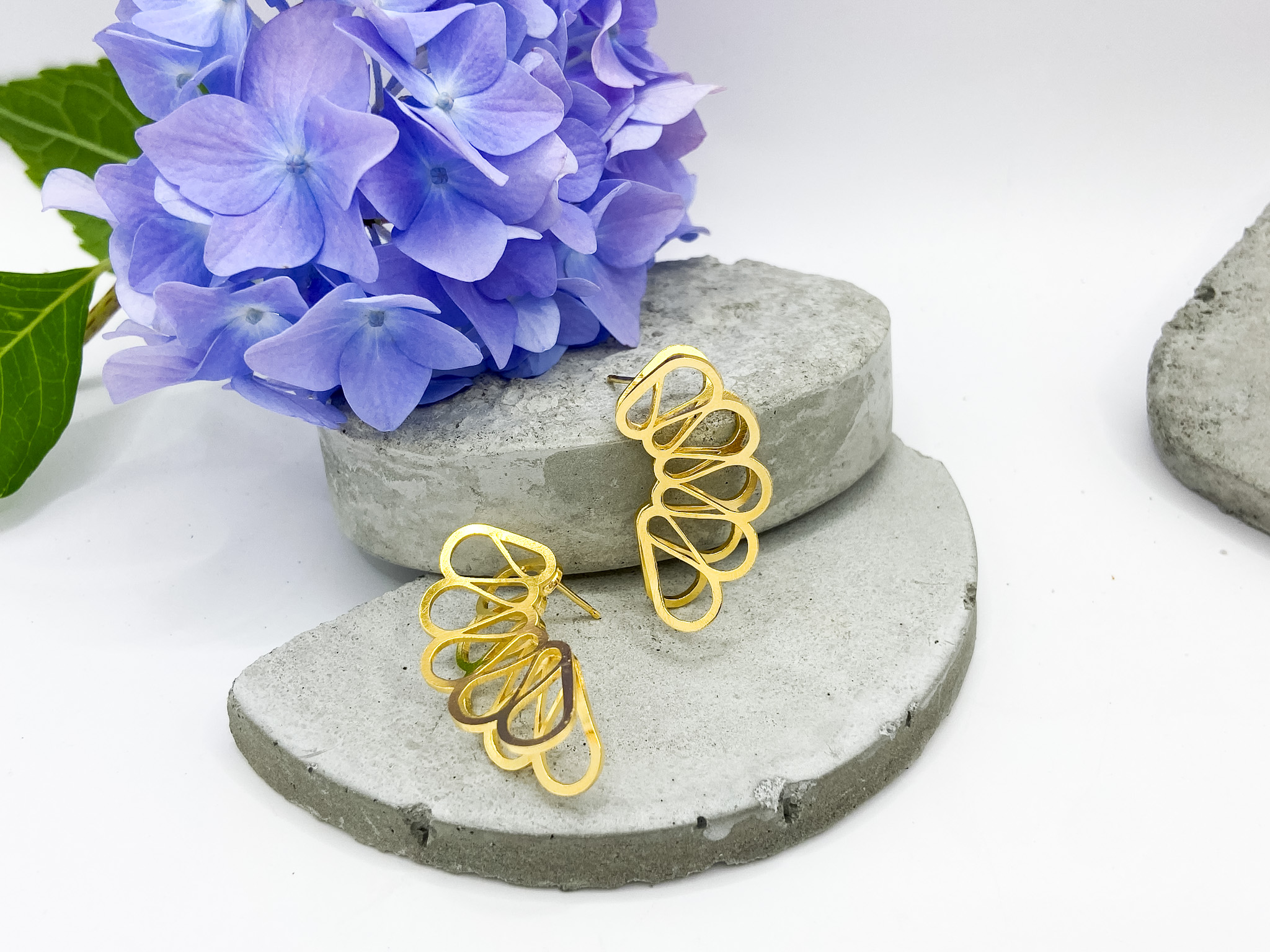 Purple hydrangea flower, two gold wire earrings, and gray stones on a white background.