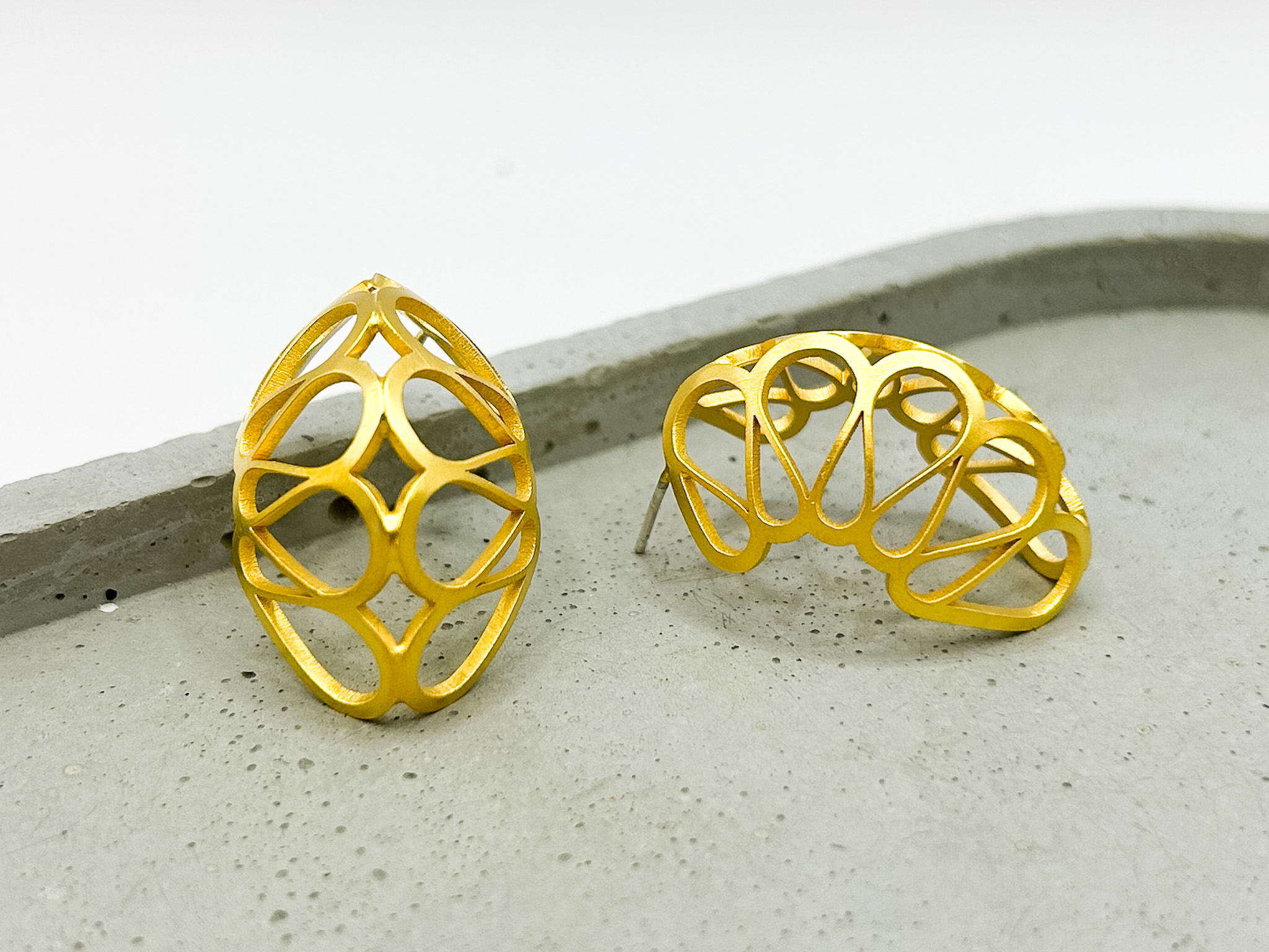 Two gold jewelry pieces with open lattice design on a gray surface, one upright and one lying down.