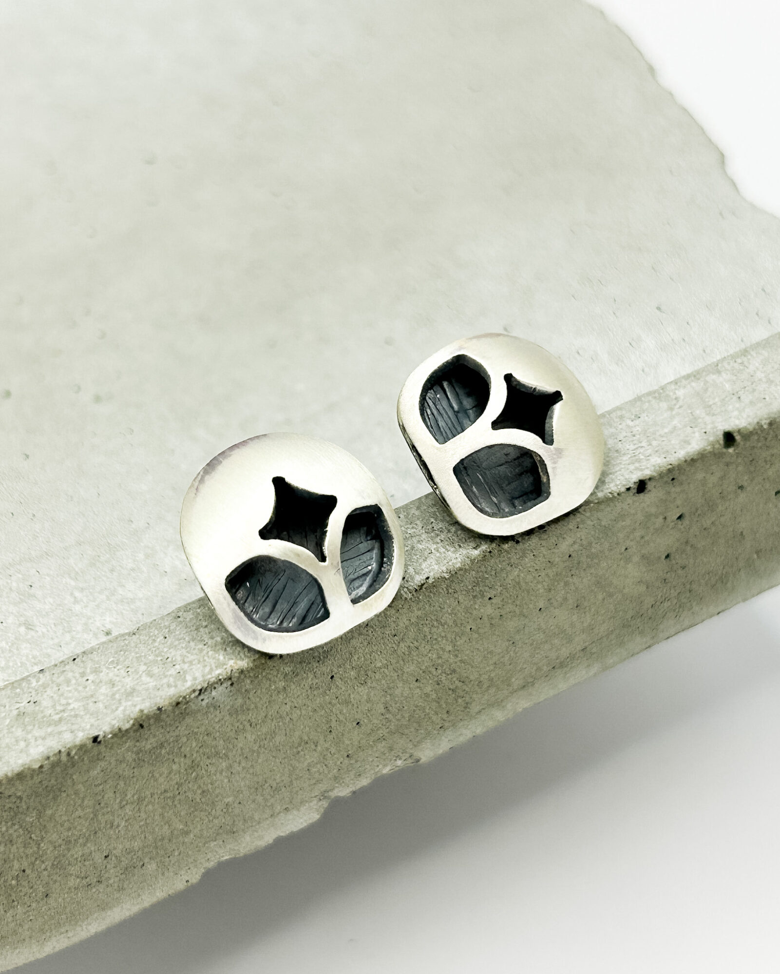 Pair of white earrings with black star-shaped cutouts, resting on a concrete surface.