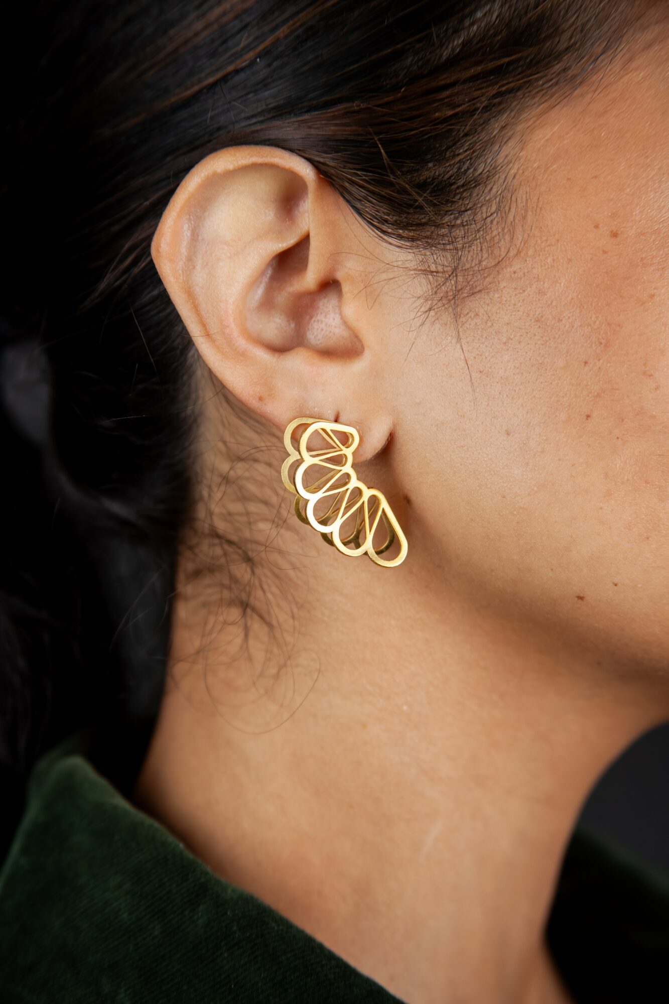 Close-up of a woman's ear with a gold earring, showing part of her face and neck.