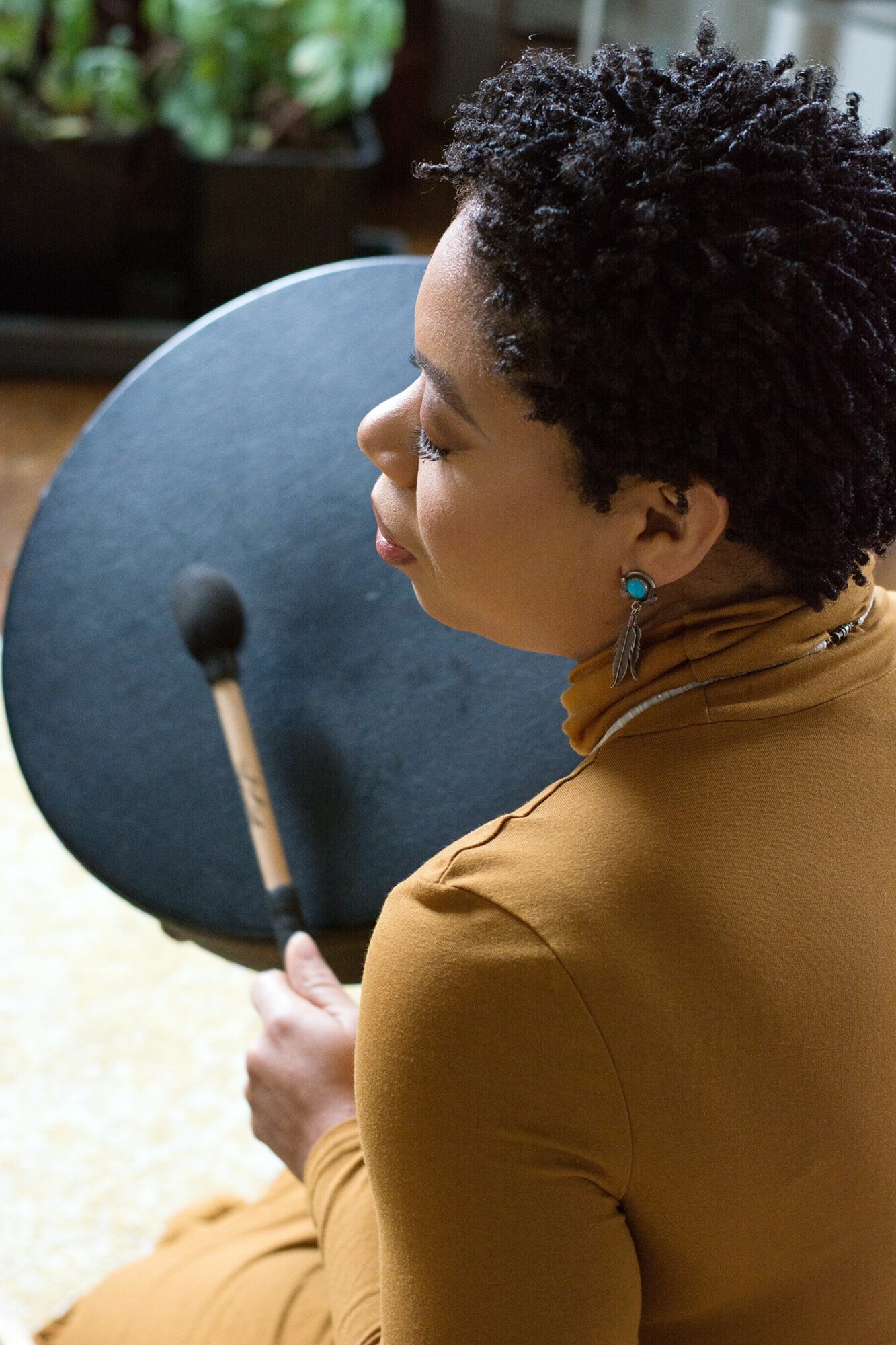 Woman with short curly hair holding a round black object, wearing a brown jacket and blue earrings.
