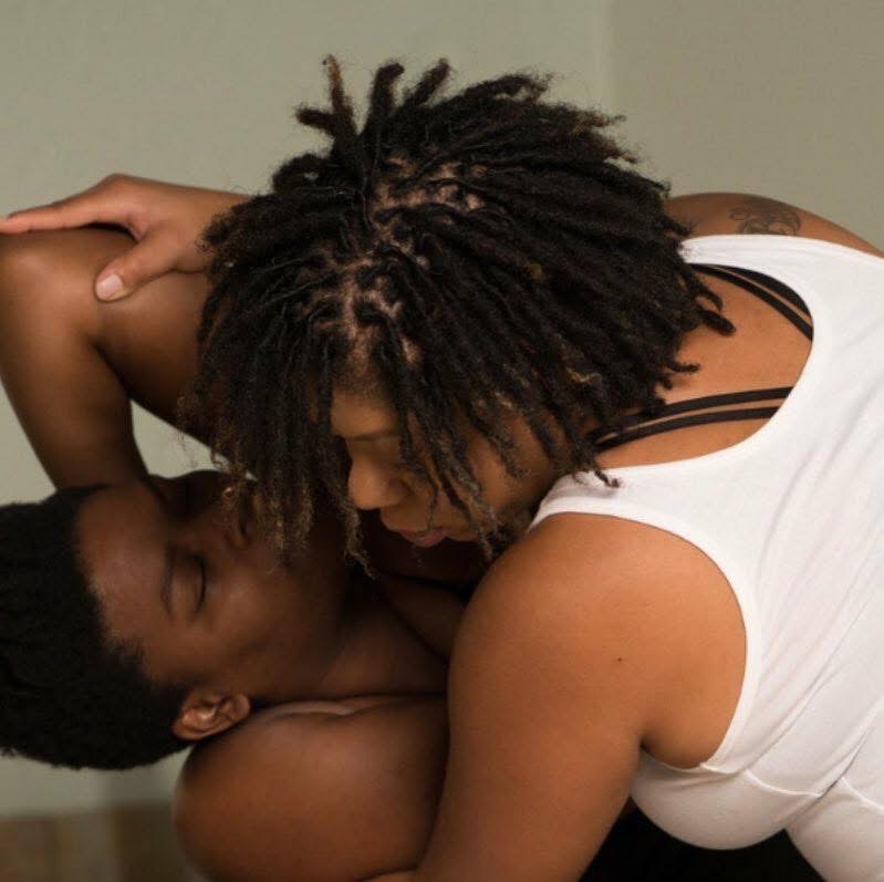 Two people close together, one with dreadlocks and the other with short hair, in an intimate pose.