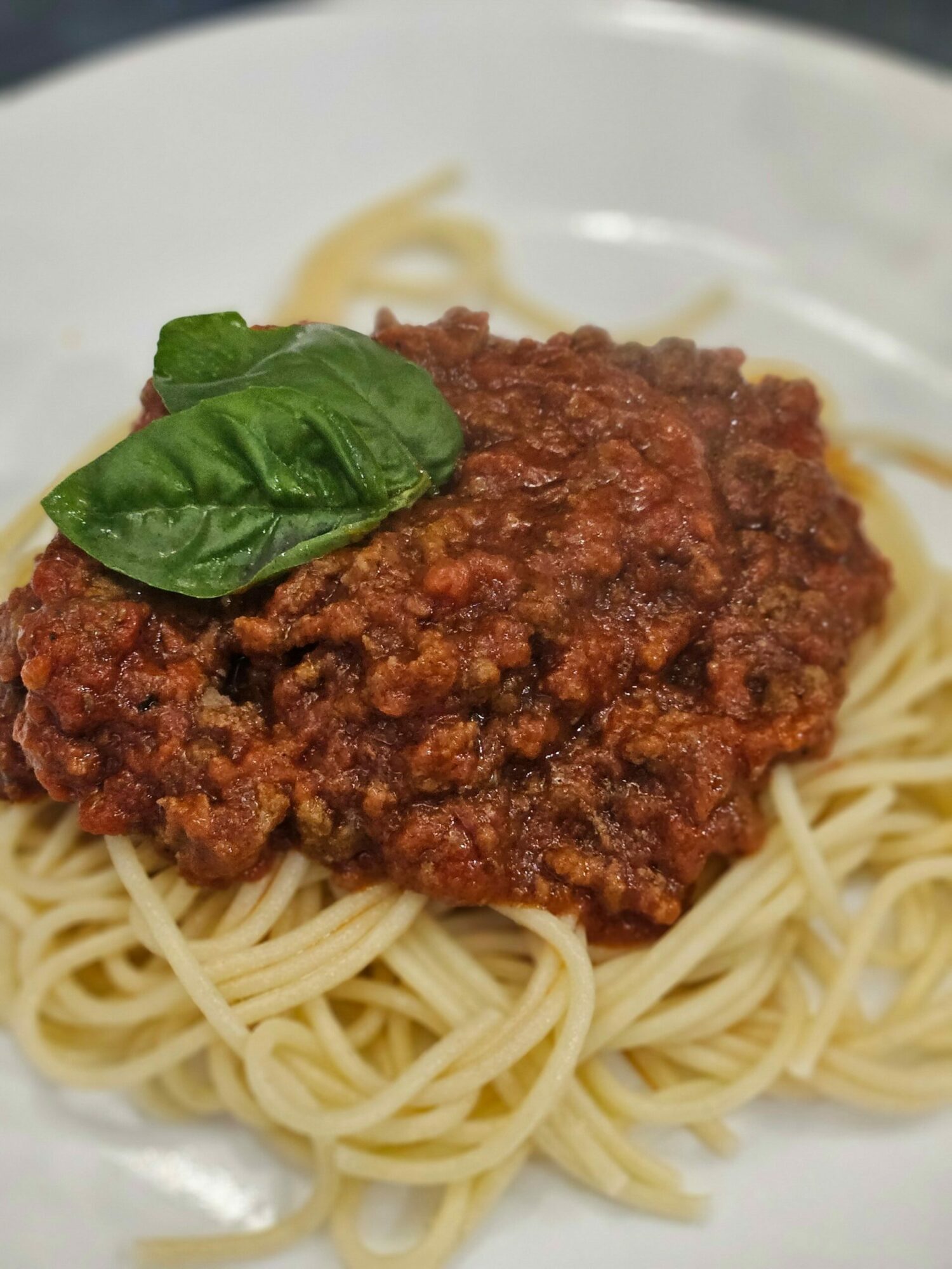 Spaghetti with meat sauce and a basil leaf on top, served on a white plate.
