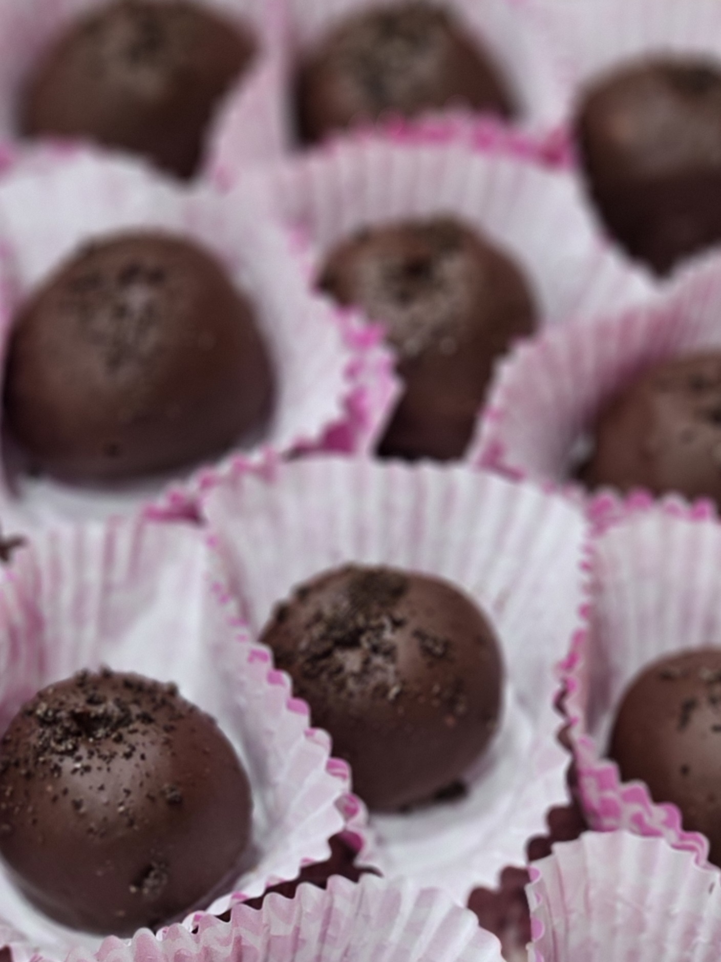 Close-up of chocolate truffles in pink and white paper cups, arranged closely together.