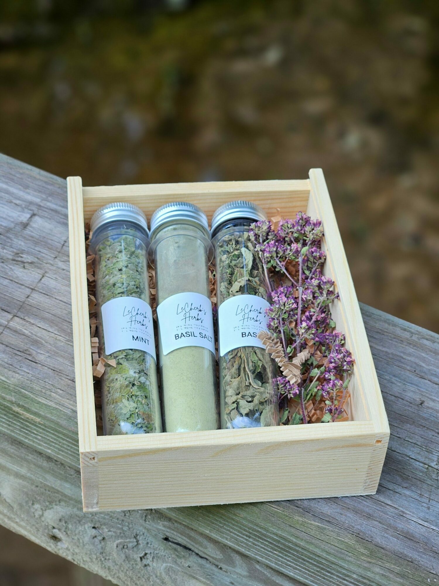 Wooden box with glass jars containing herbs and dried flowers, placed on a wooden surface outdoors.