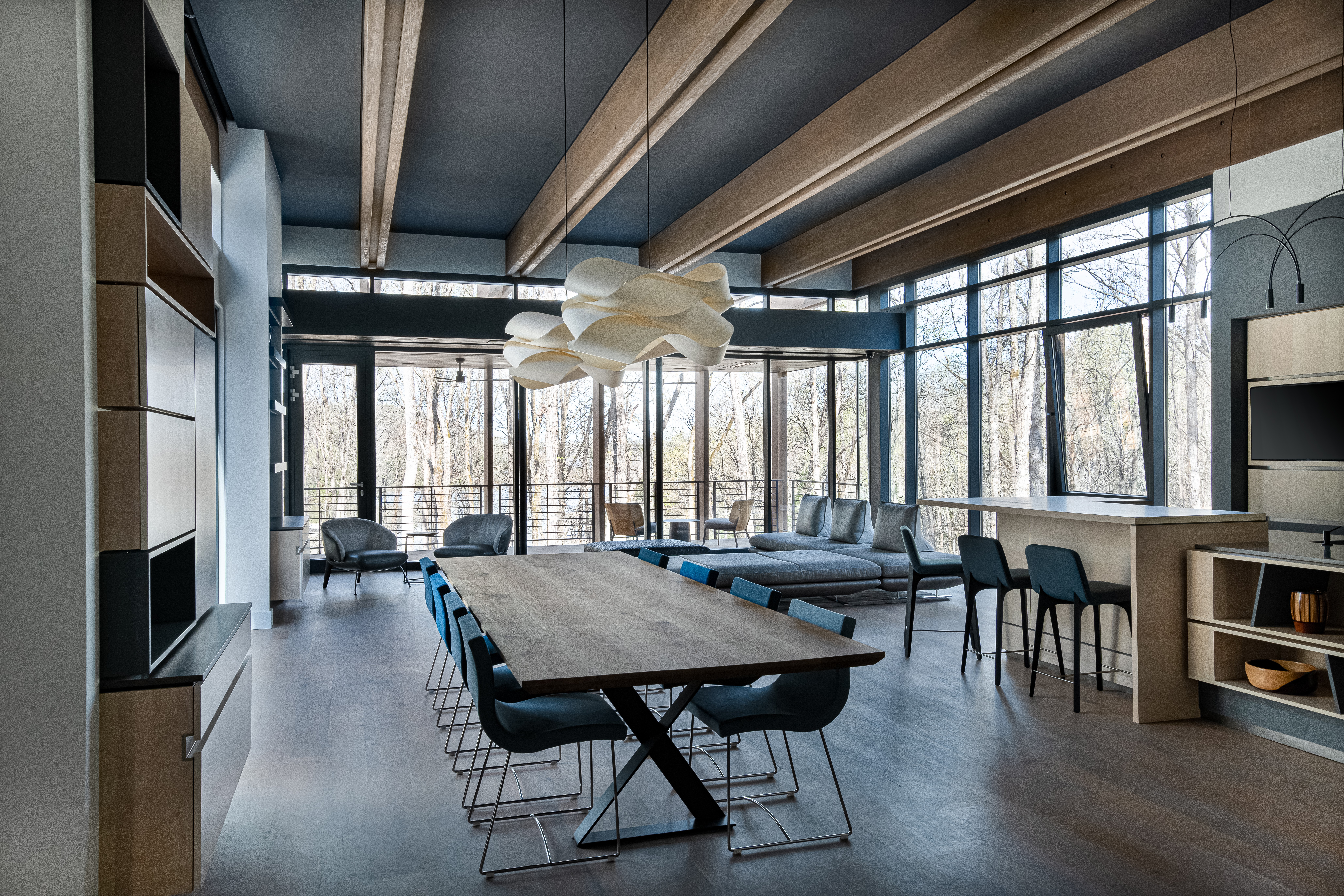 Modern lounge with large windows, seating, and a central table in a spacious room.
