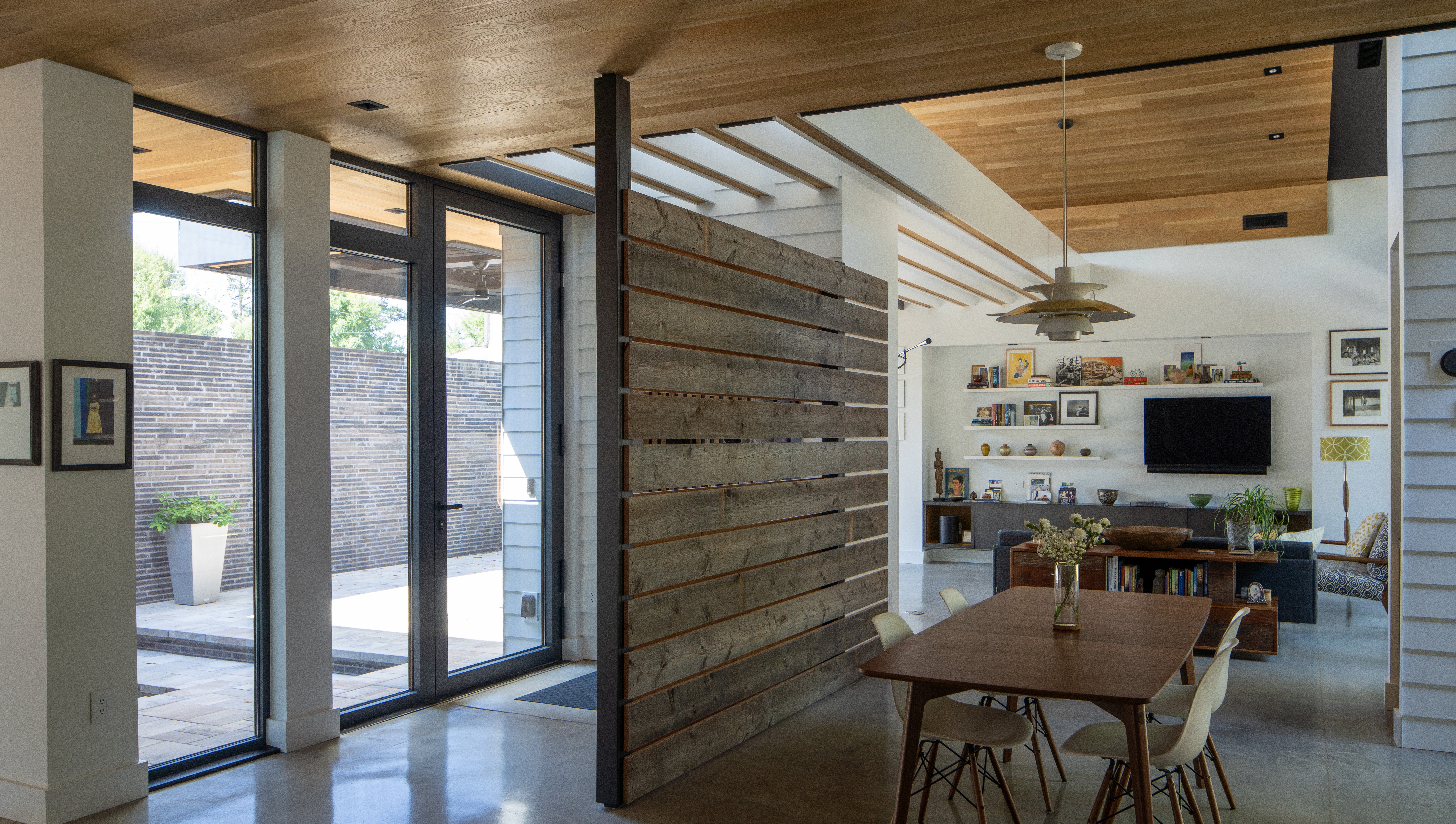 Open-concept living and dining area with large windows, wooden ceiling, and modern furniture.