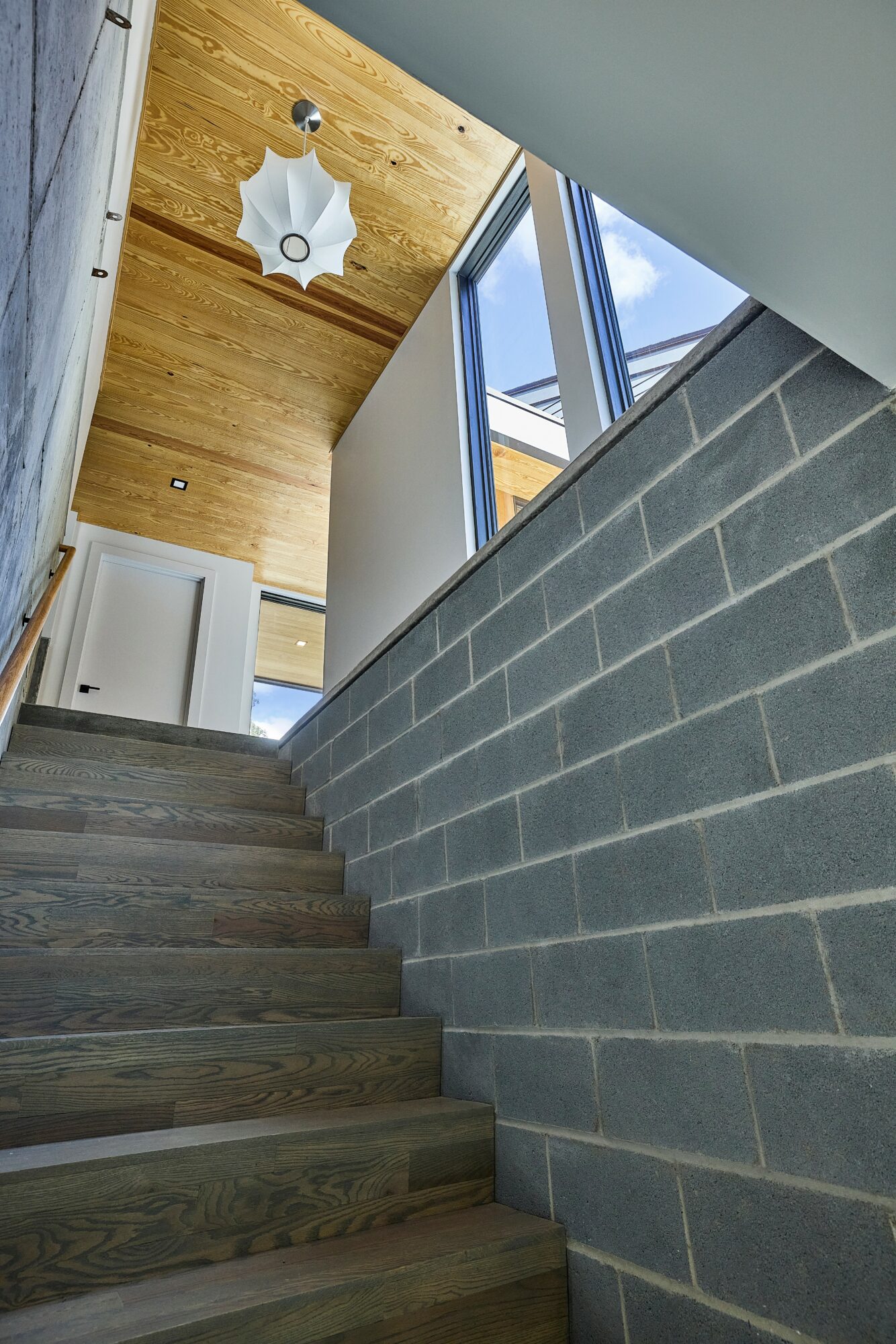 View of staircase with wooden steps, gray brick wall, large window, and ceiling with wooden paneling and a light fixture.