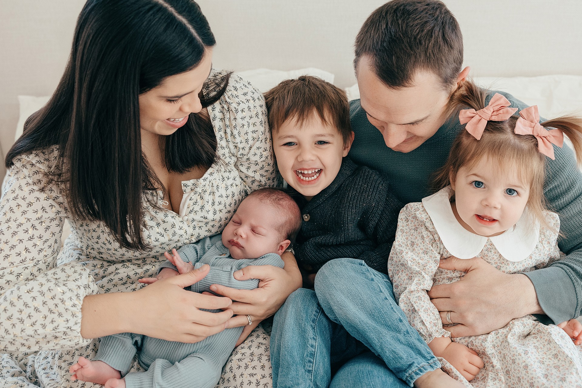 Family of five with two young children and two babies, smiling and sitting together indoors.