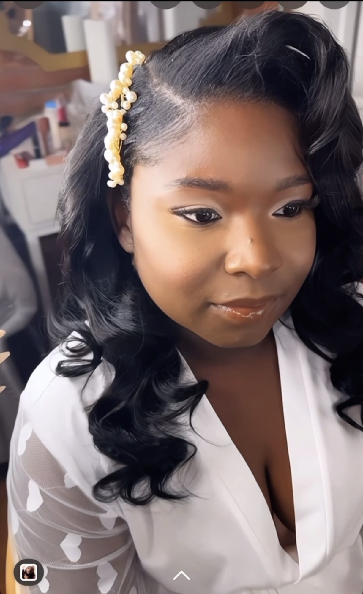 Young woman with styled black hair and pearl hair accessory, wearing a white top, looking down slightly.