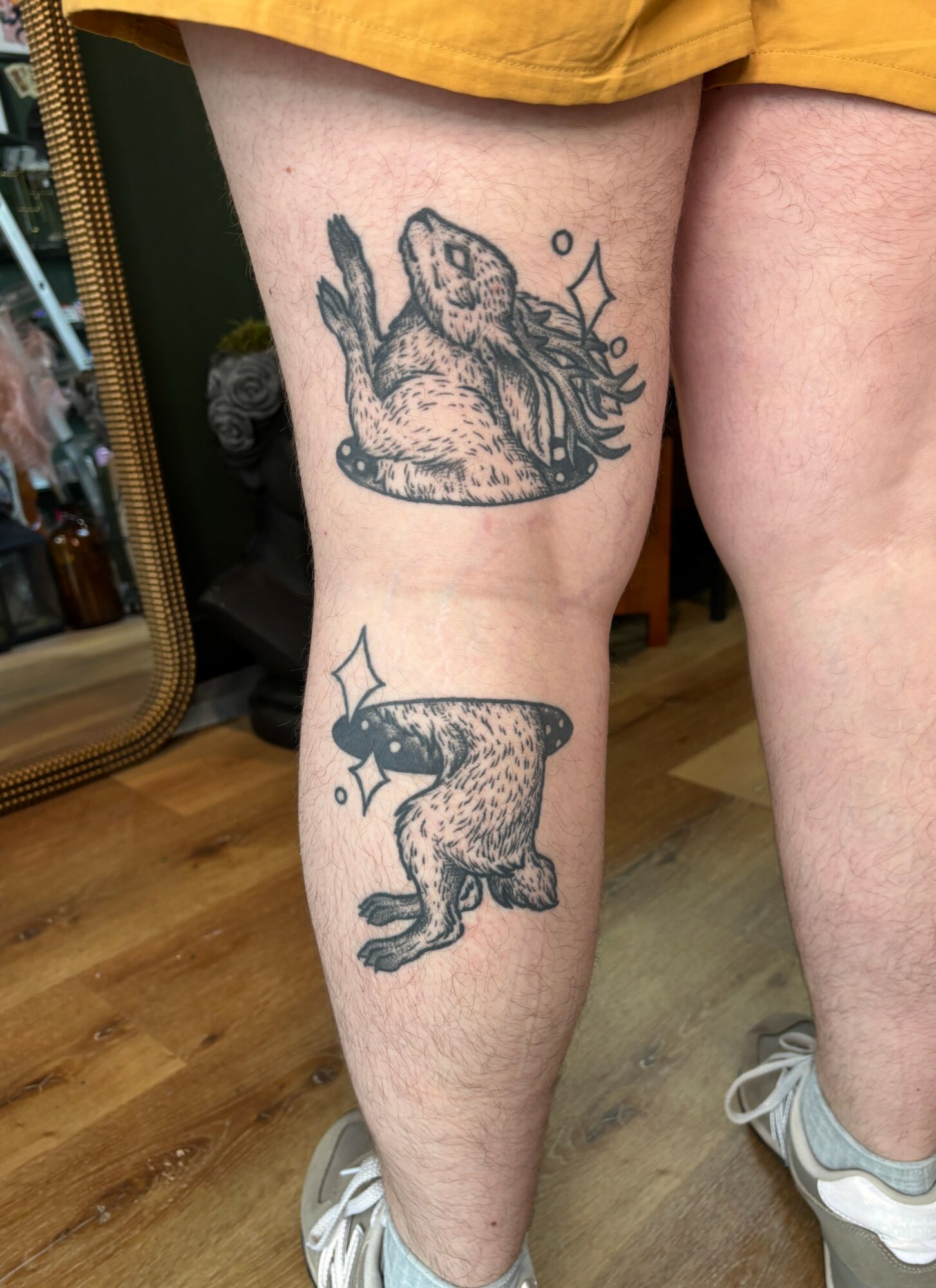 Tattoo of a dog and a frog on person's thigh, with decorative sparkles around them.