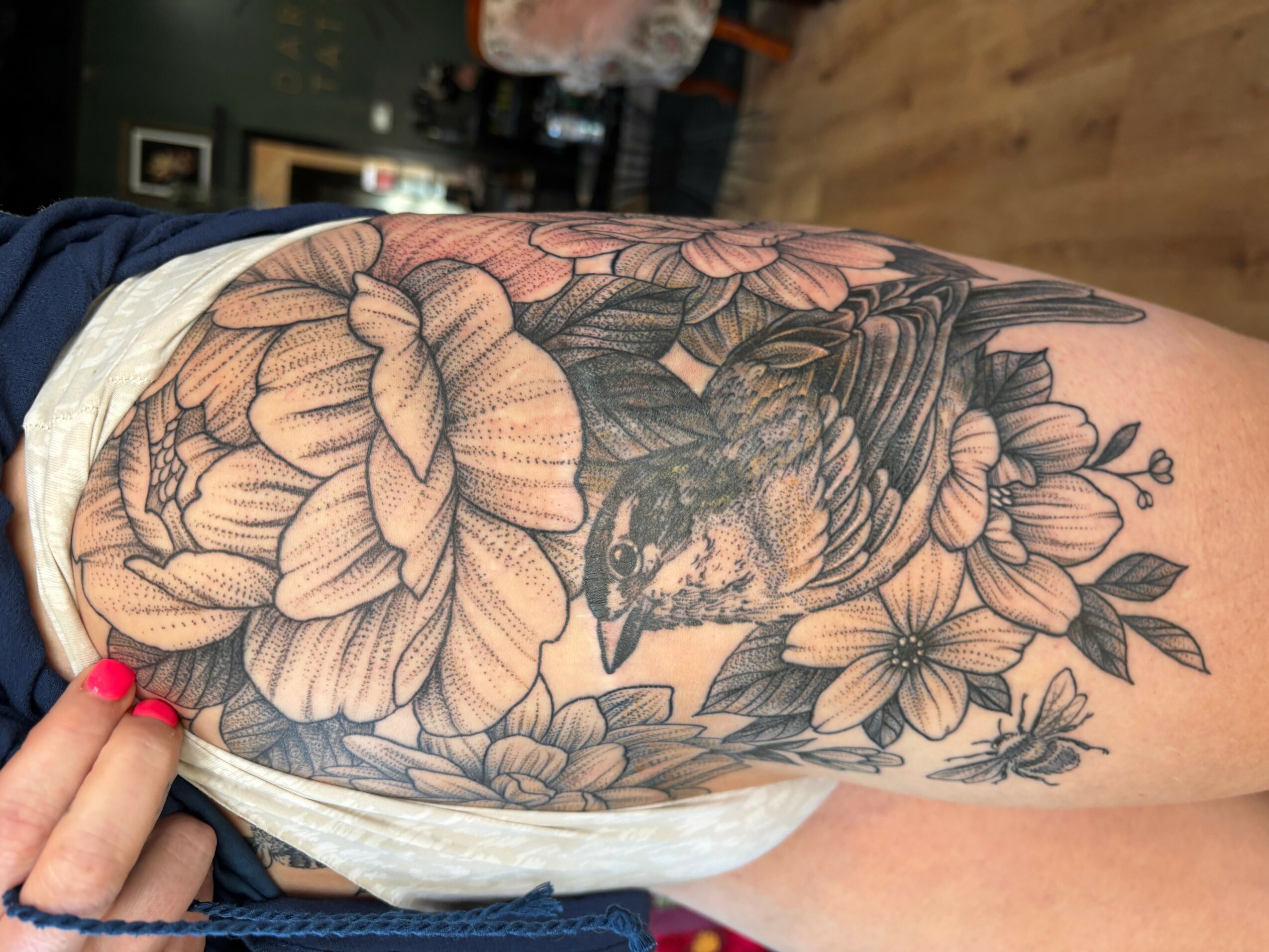 Detailed black and gray floral tattoo with a bird on a person's thigh, featuring large flowers and leaves.