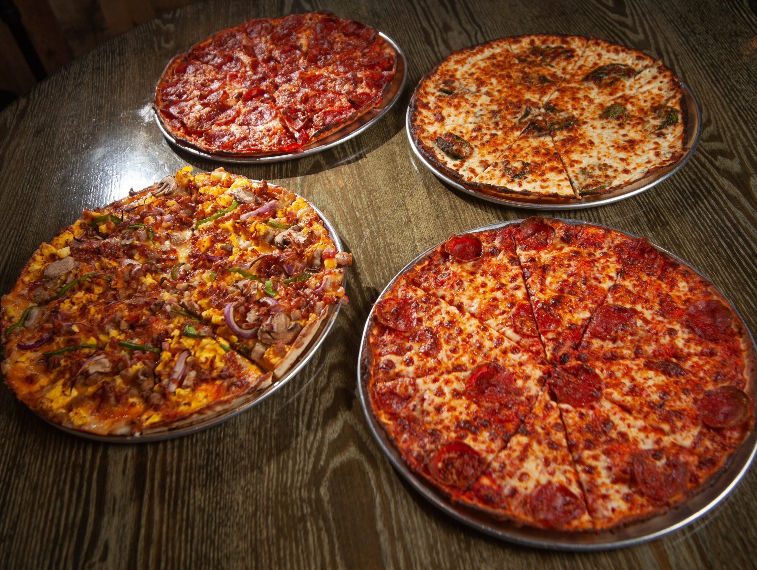 Four pizzas on plates, two with pepperoni, one with meat toppings, one plain cheese, on a wooden table.