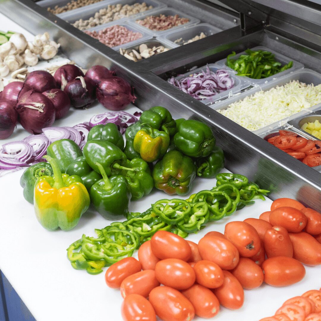 Fresh vegetables including red onions, green bell peppers, yellow bell peppers, sliced green peppers, and tomatoes on a counter.