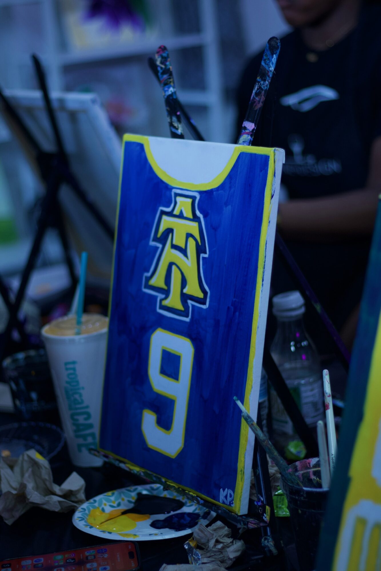 A blue and yellow sign with the number nine and a logo, surrounded by cups, bottles, and art supplies.