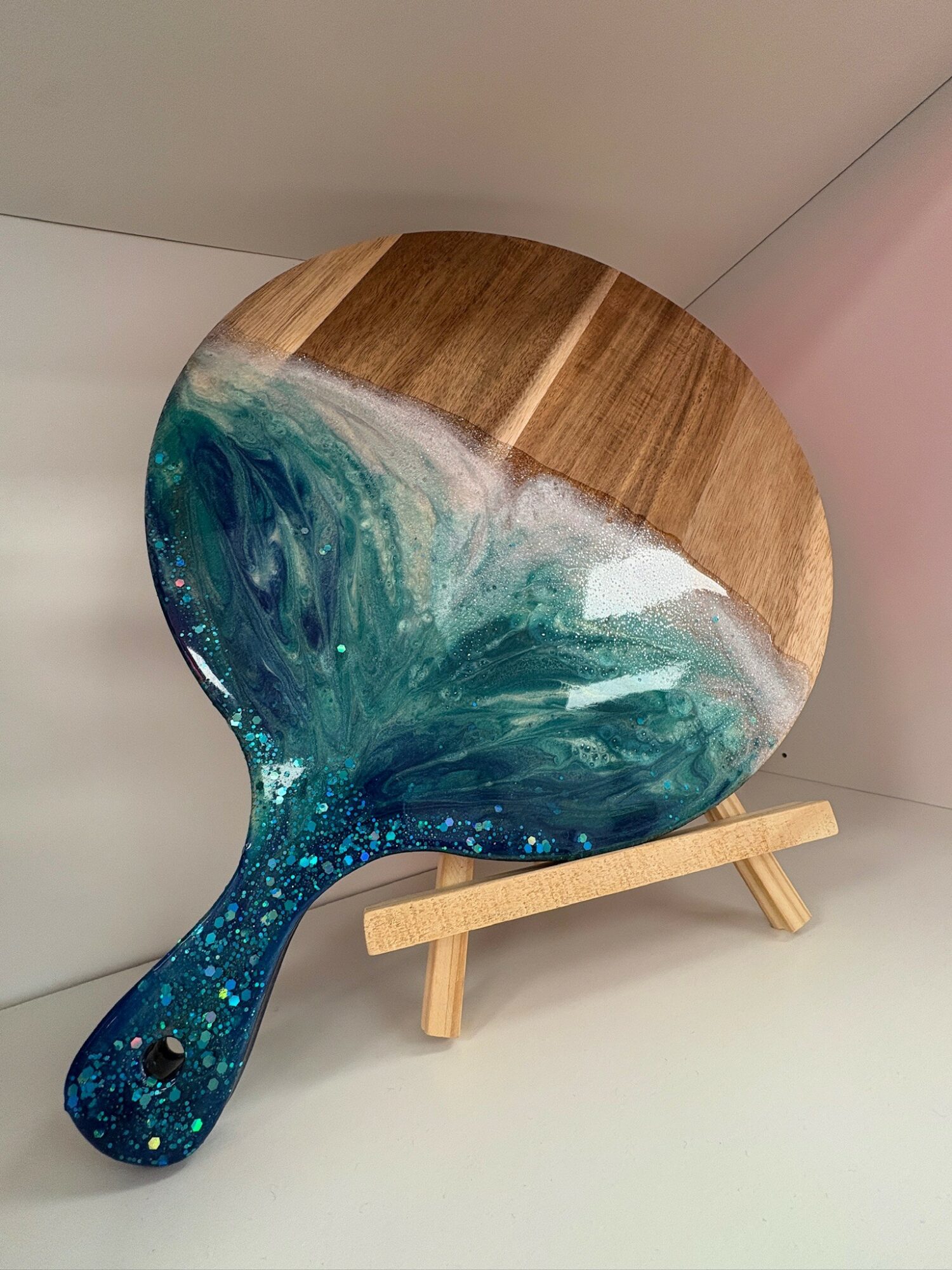 Round decorative tray with ocean wave design, placed on a small wooden stand, against a plain background.