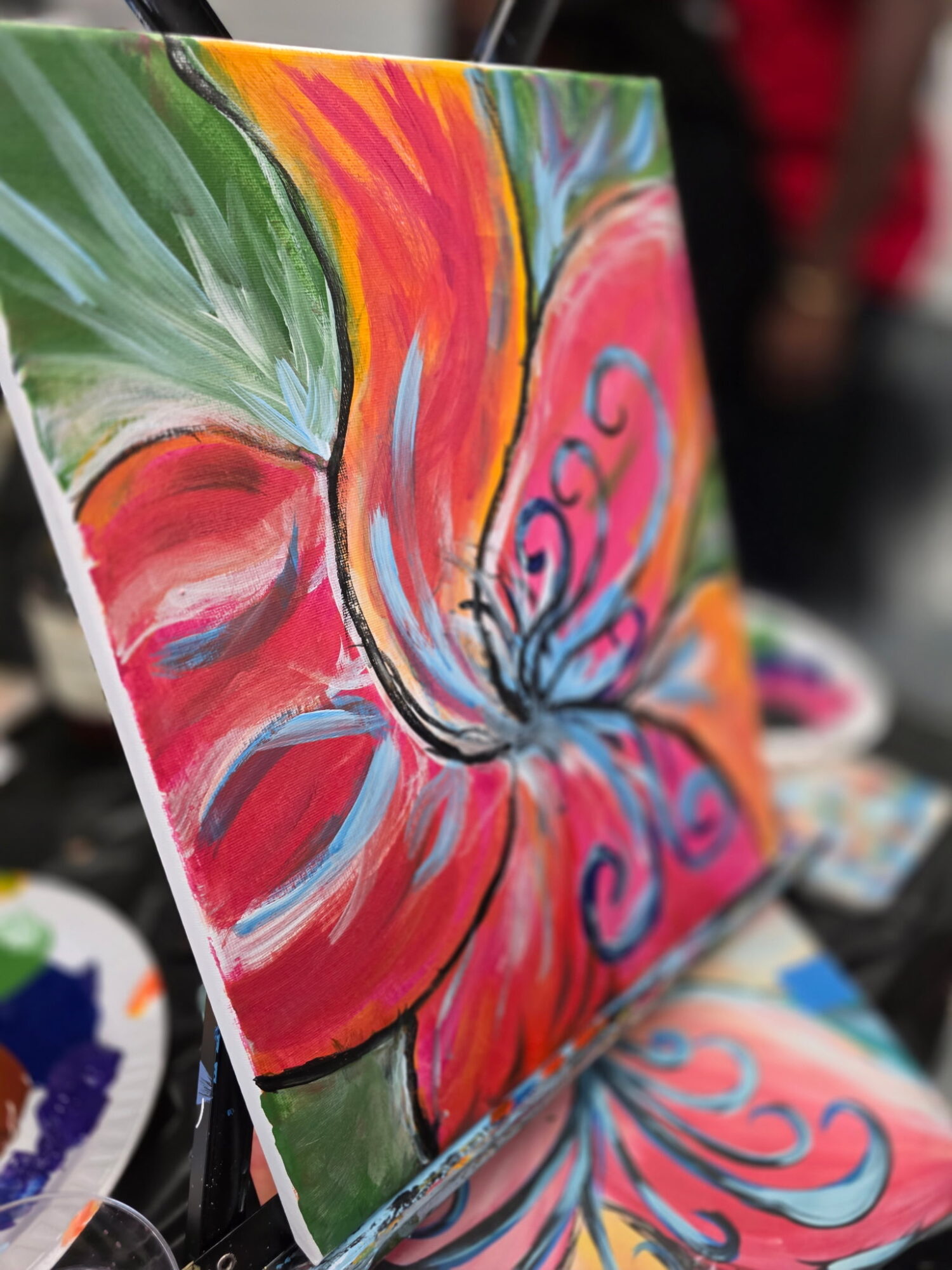 Colorful abstract flower painting with vibrant red, orange, green, and blue hues, featuring swirling patterns and bold brushstrokes.