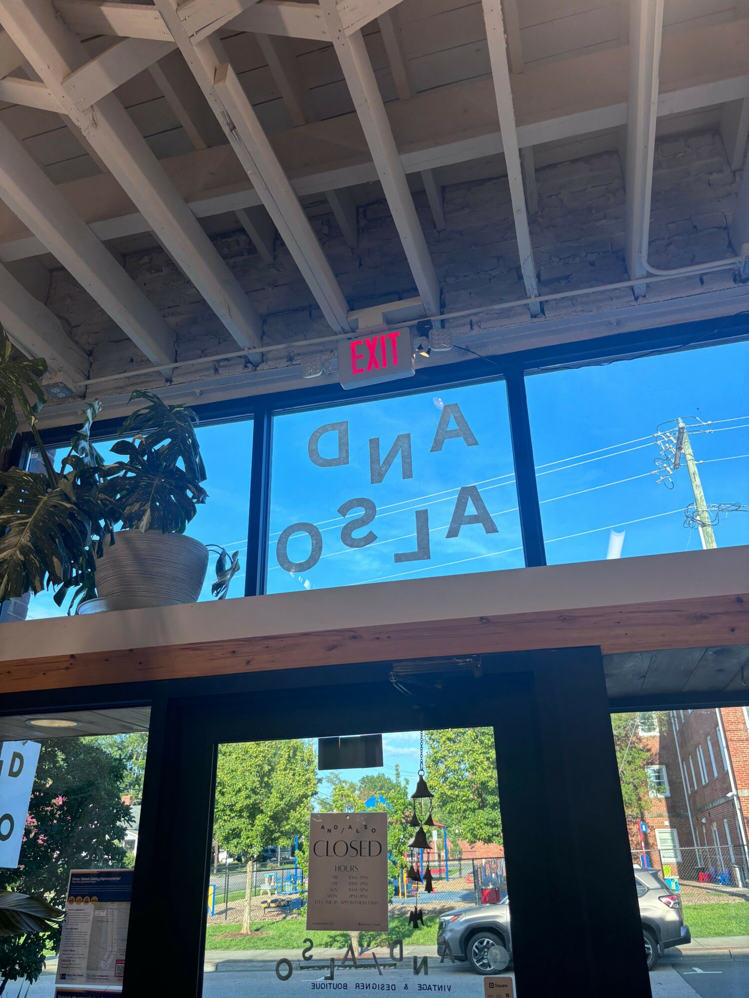 View through a window showing blue sky, power lines, and a sign with partially visible text, with a plant inside.